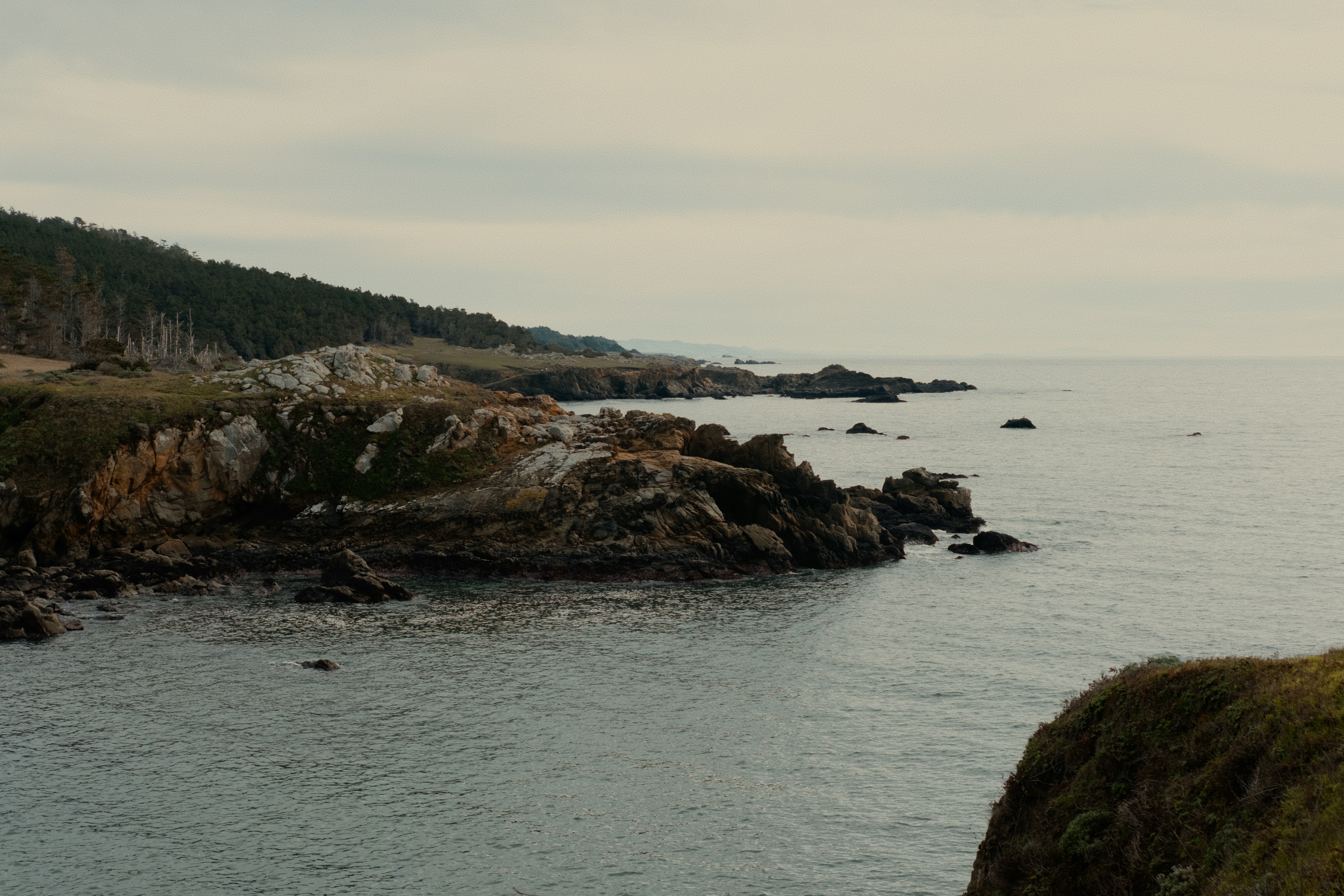 Rocky coastline with calm ocean under cloudy sky