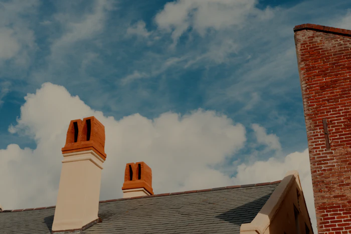 Two brick chimney stacks on a rooftop against a cloudy sky
