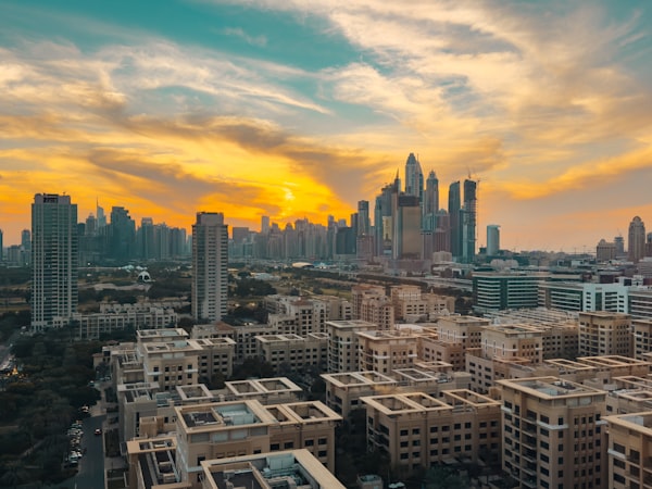 Dubai Marina towers rise behind low-rise residential blocks under a gold sunset sky.