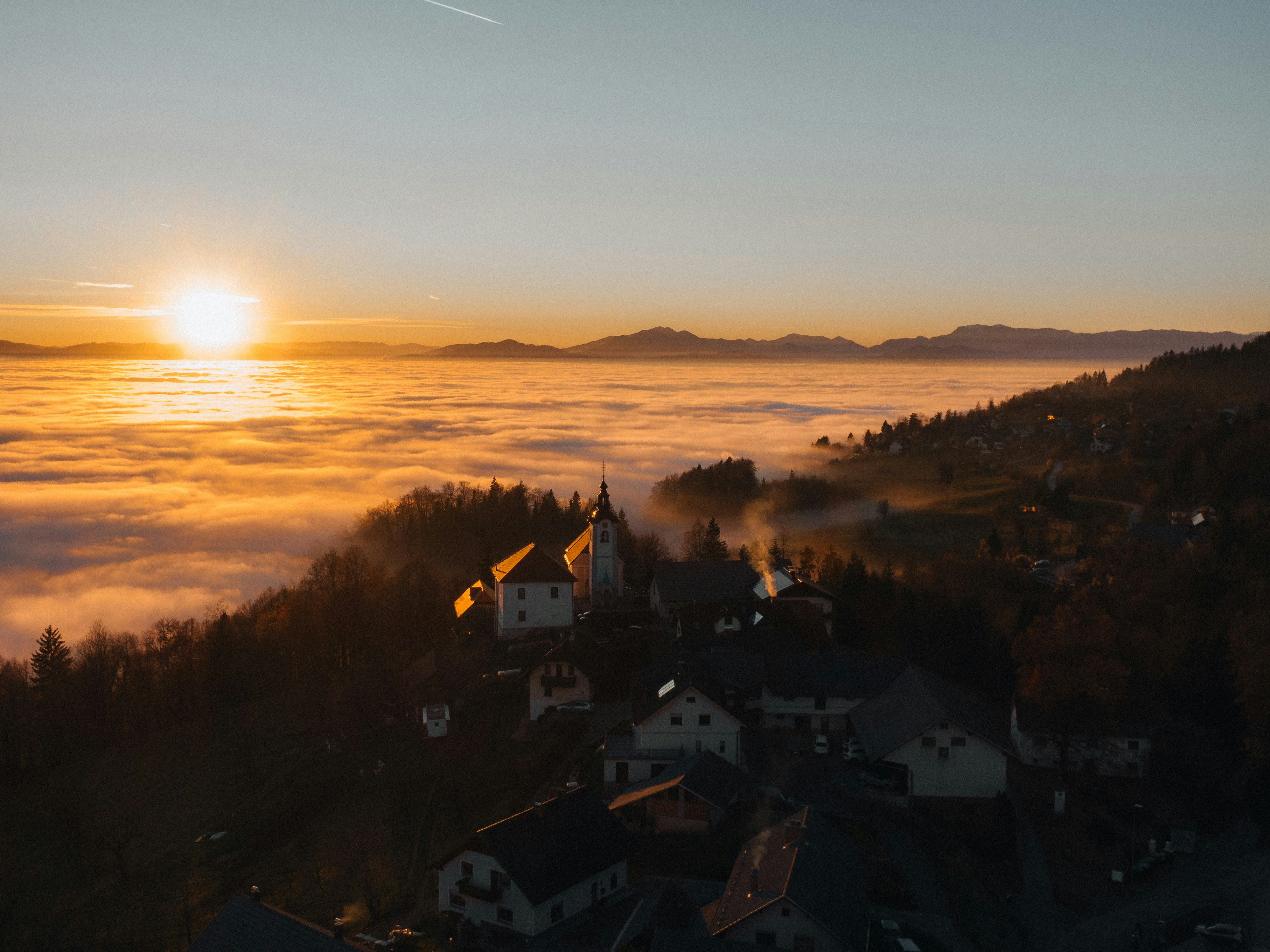 Village nestled in fog at sunrise with distant mountains.