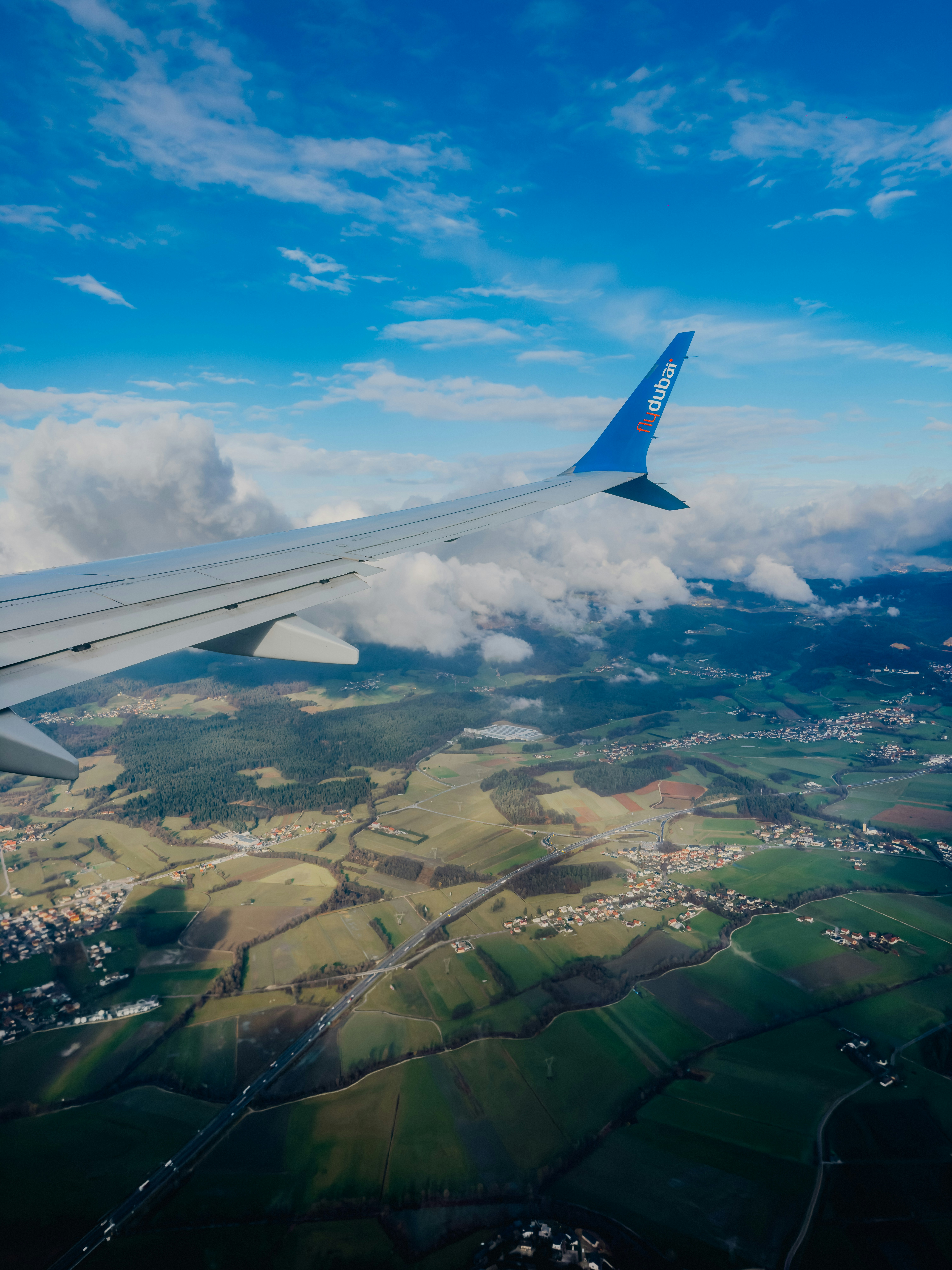 Airplane wing over green landscape and clouds
