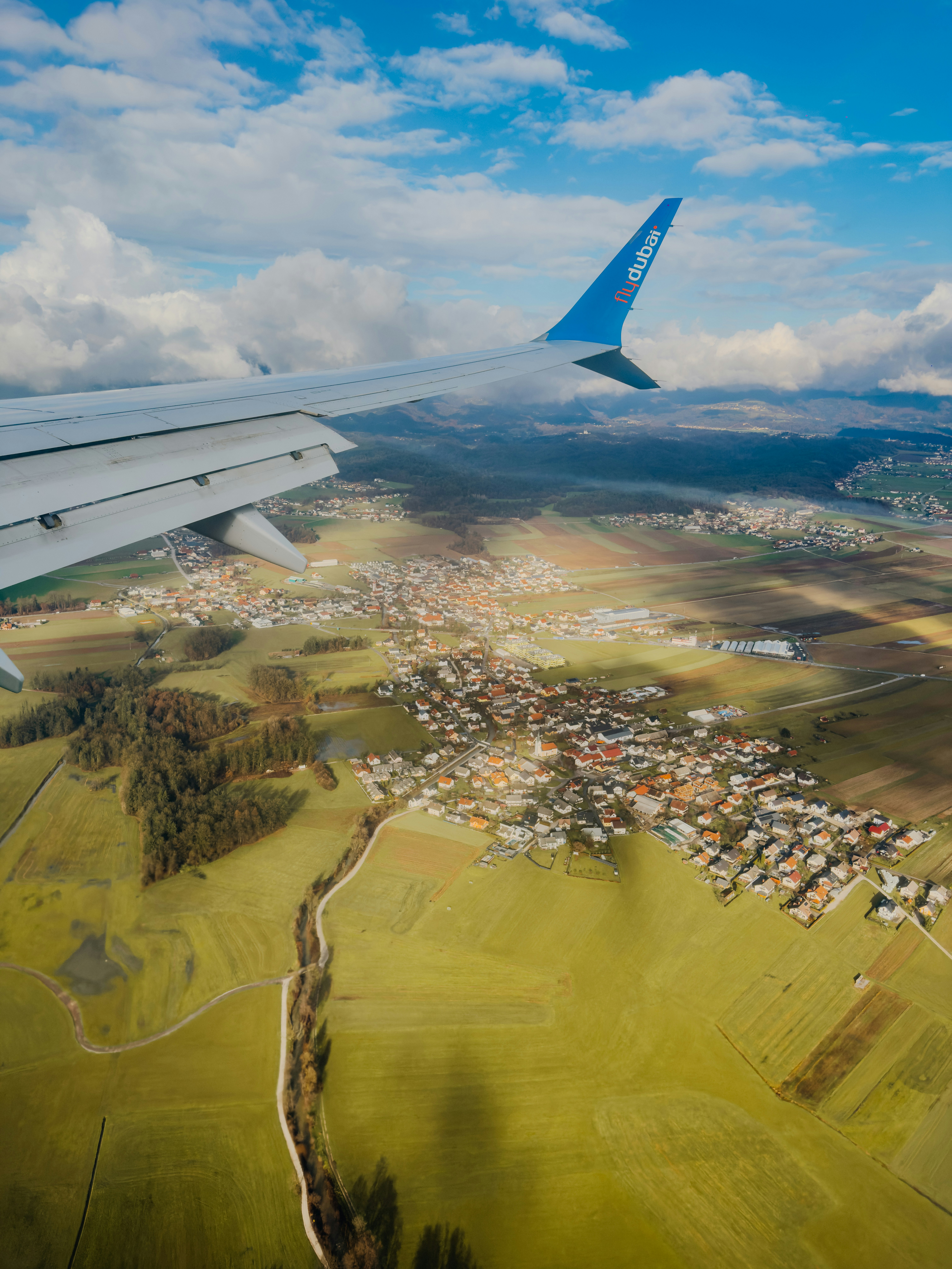Airplane wing over a rural village under cloudy sky