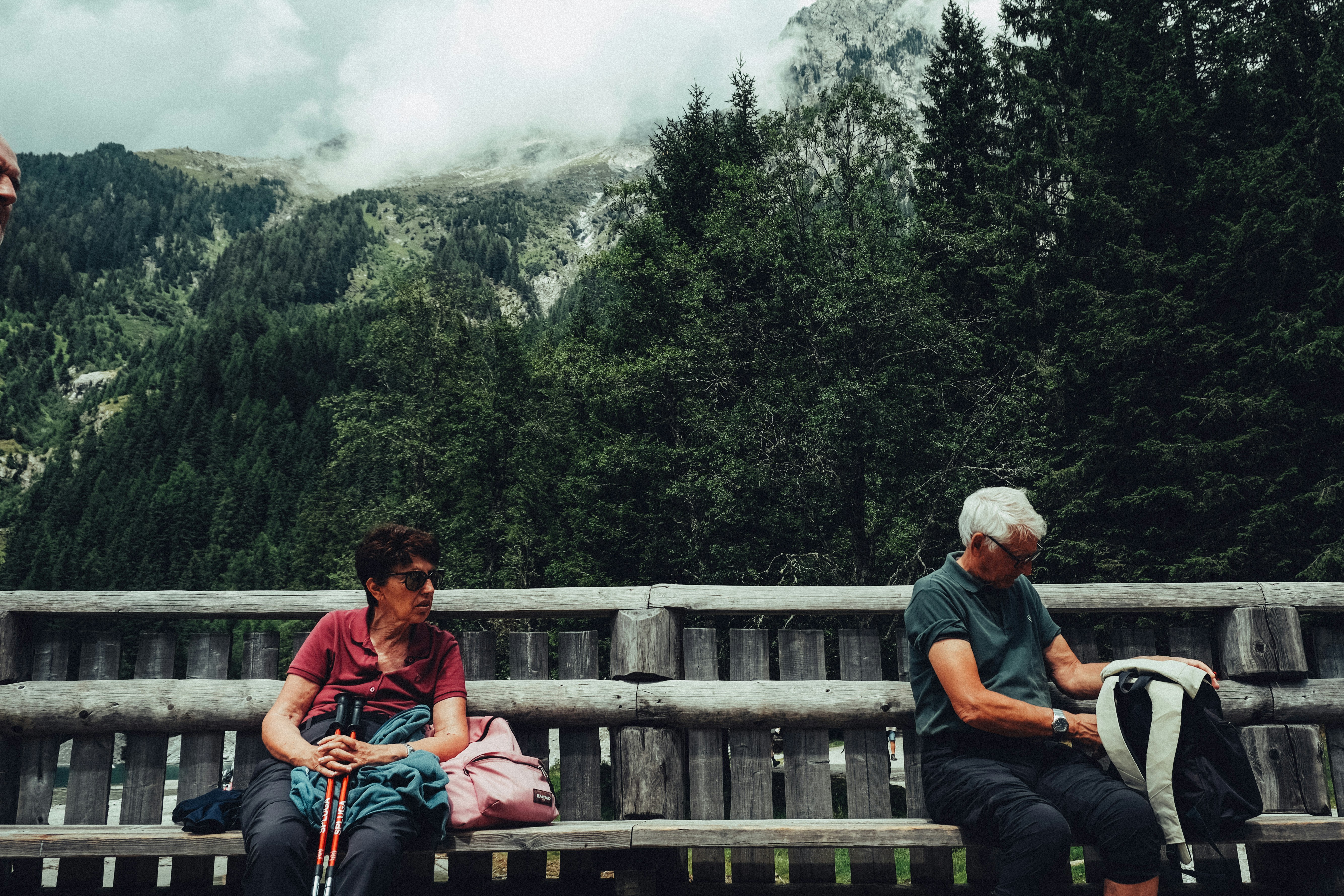 Two people resting on a bench with mountains behind them
