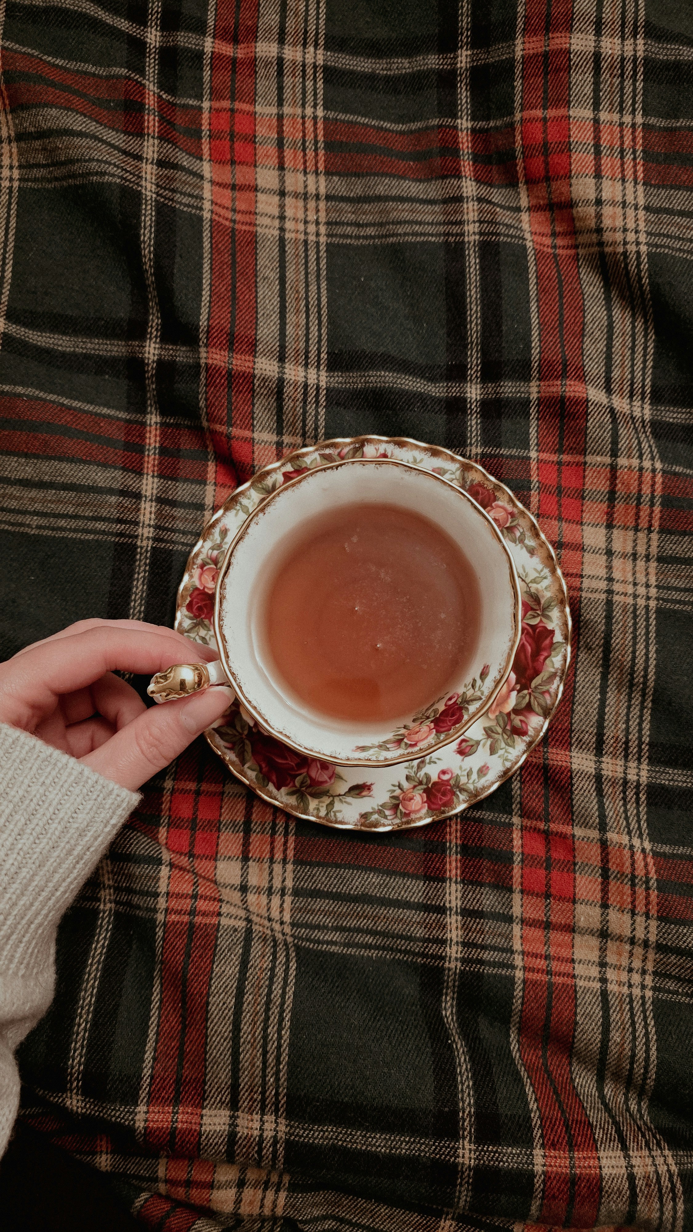 Une main tient une tasse de thé fleurie remplie de thé.