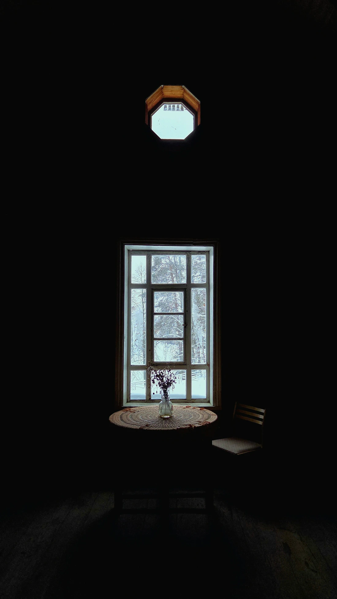 A table of flowers at a window looking onto winter trees