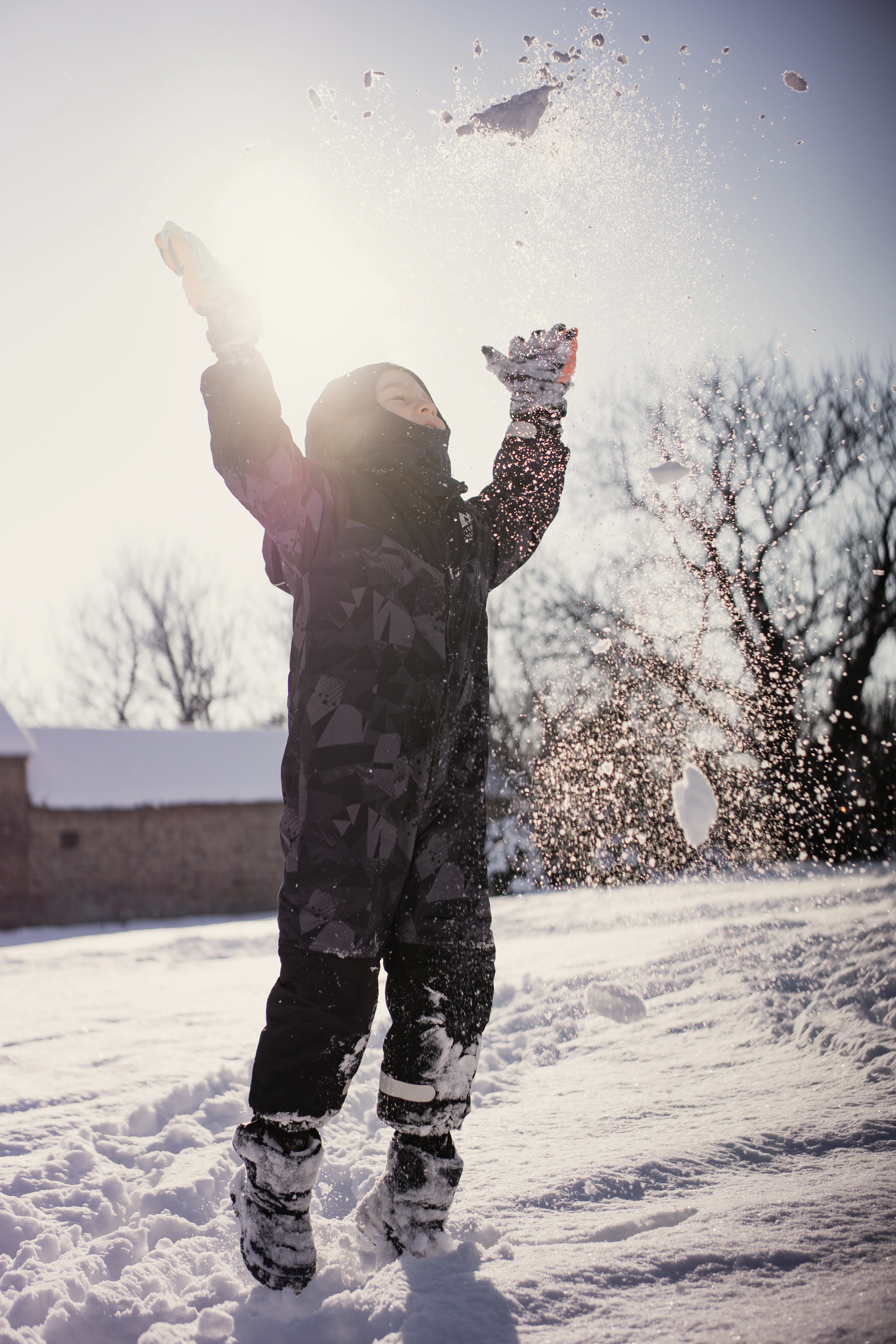 A child in a snowsuit throwing snow in the air