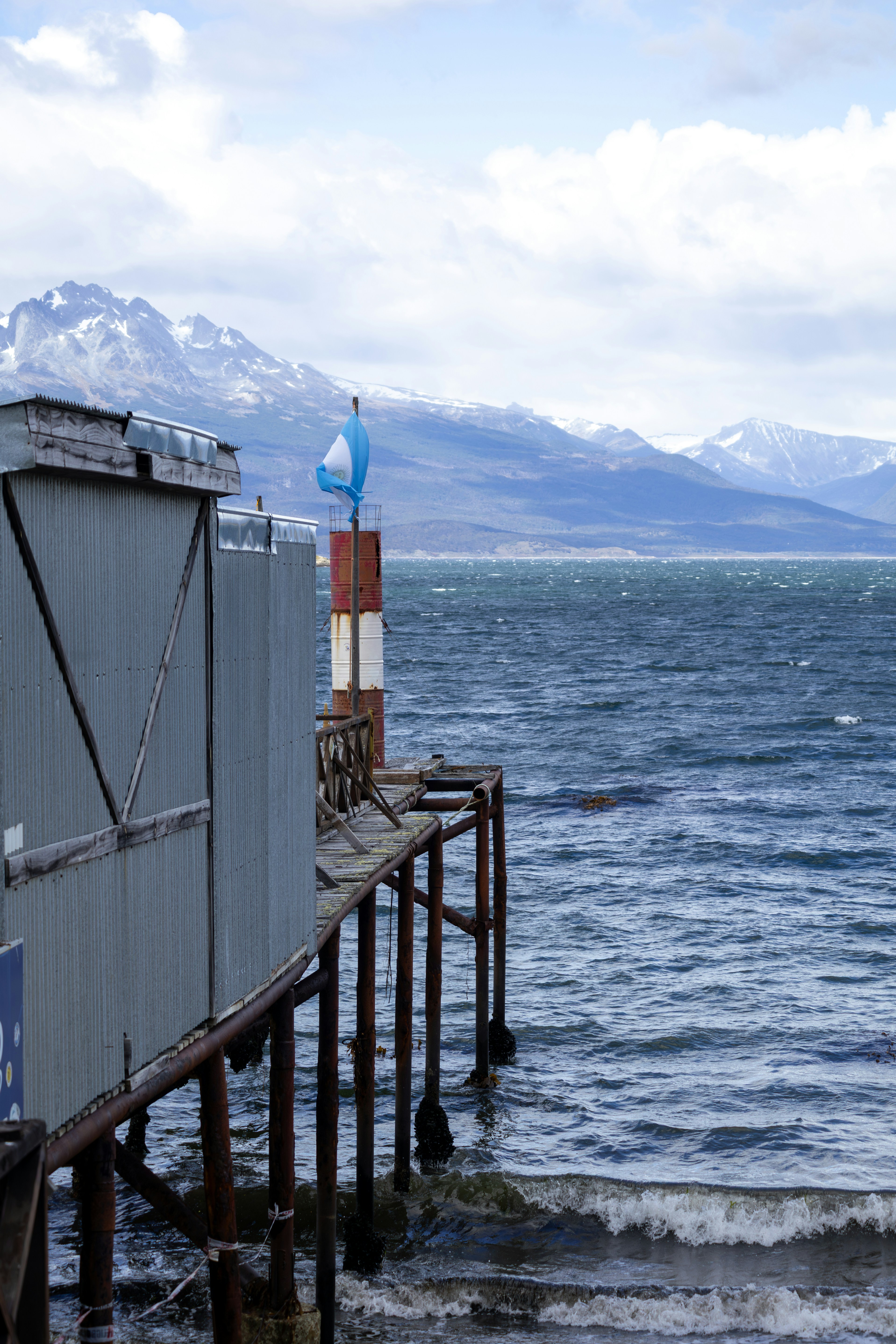 A weathered pier with an argentine flag by the sea.