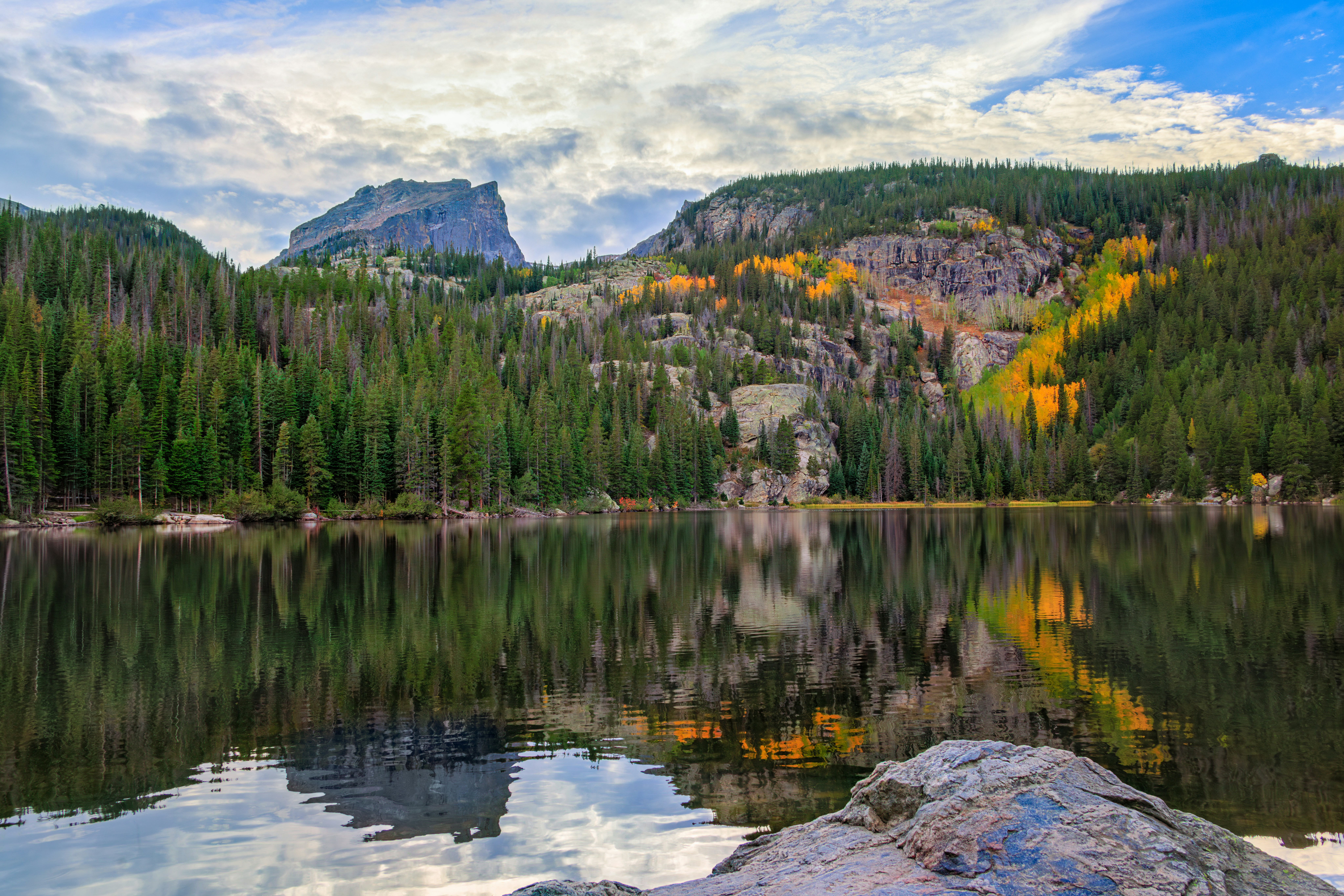 A serene mountain lake reflects trees and a cloudy sky