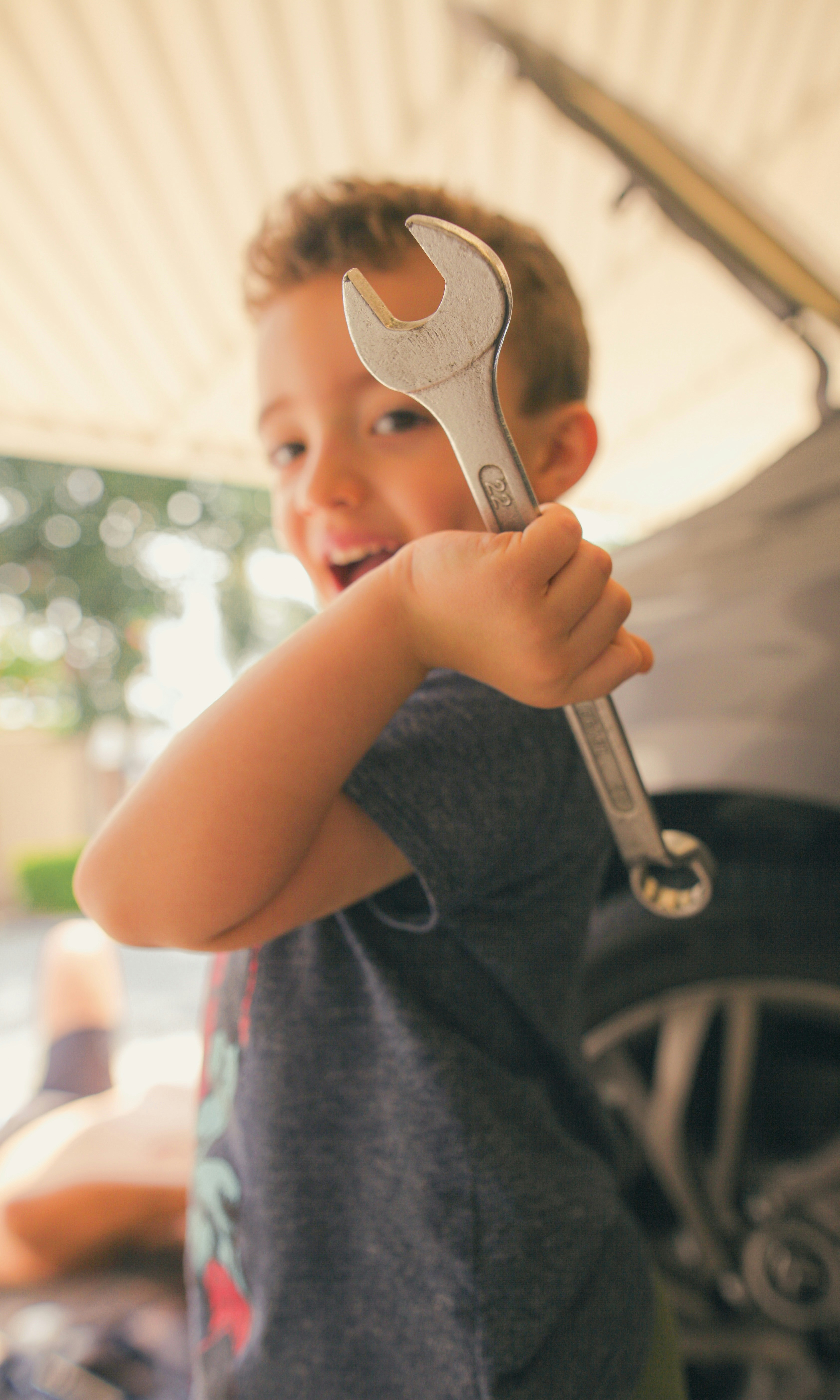 Young boy holding a wrench with a car in background