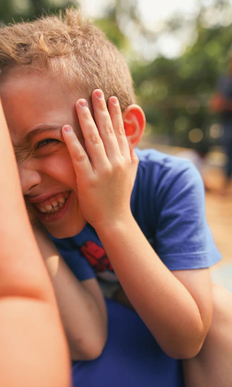 A young boy laughs while covering his face.