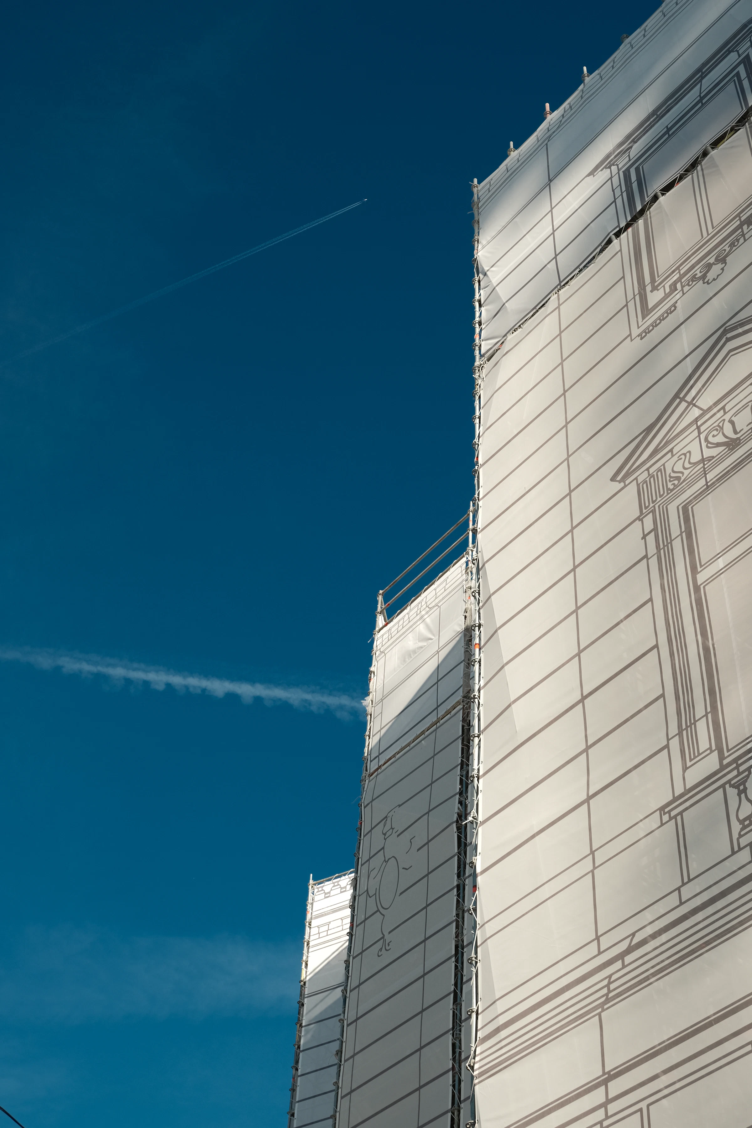 Apartment building facade under maintenance, wrapped in scaffolding against a bright blue sky