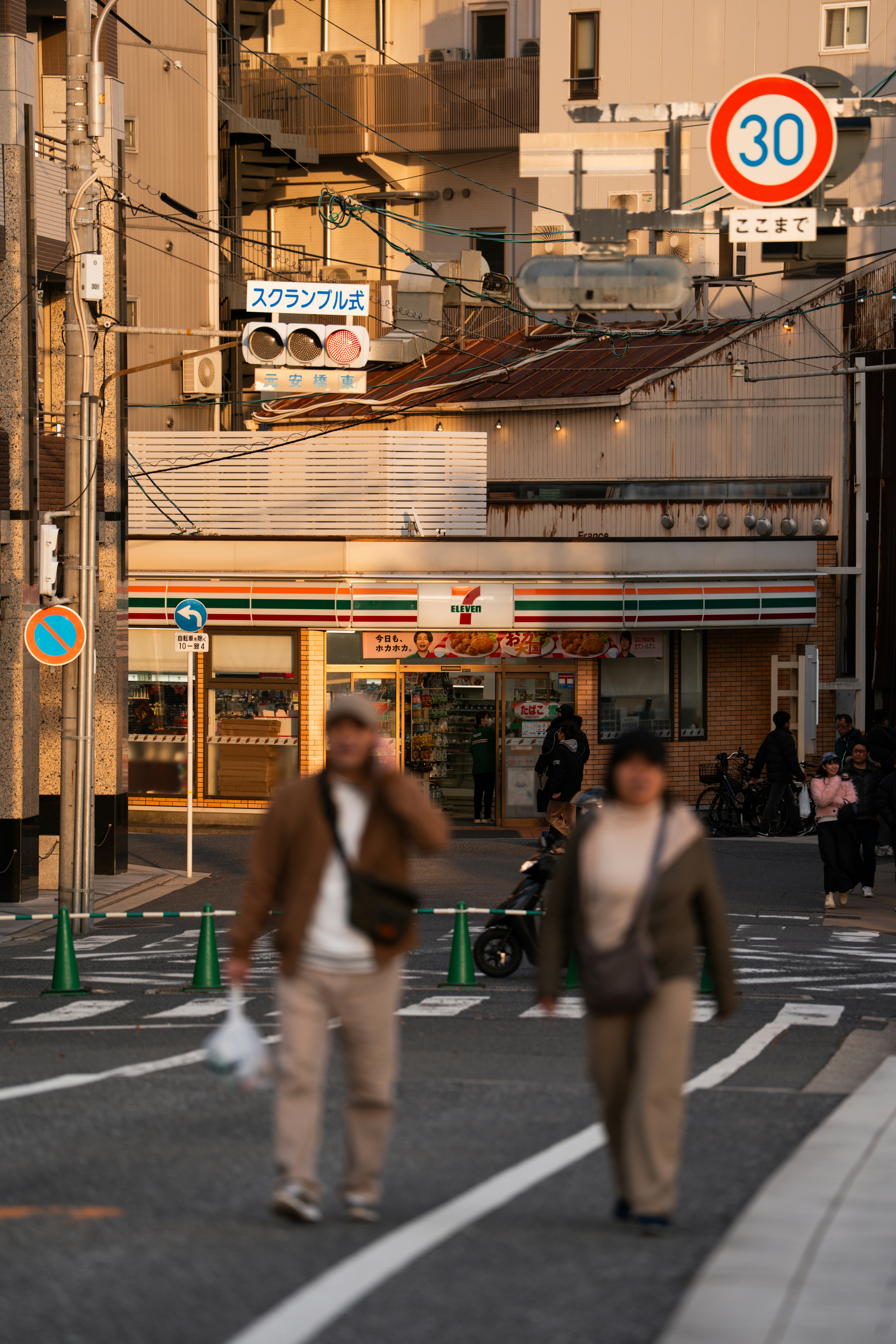 People crossing street in front of convenience store.