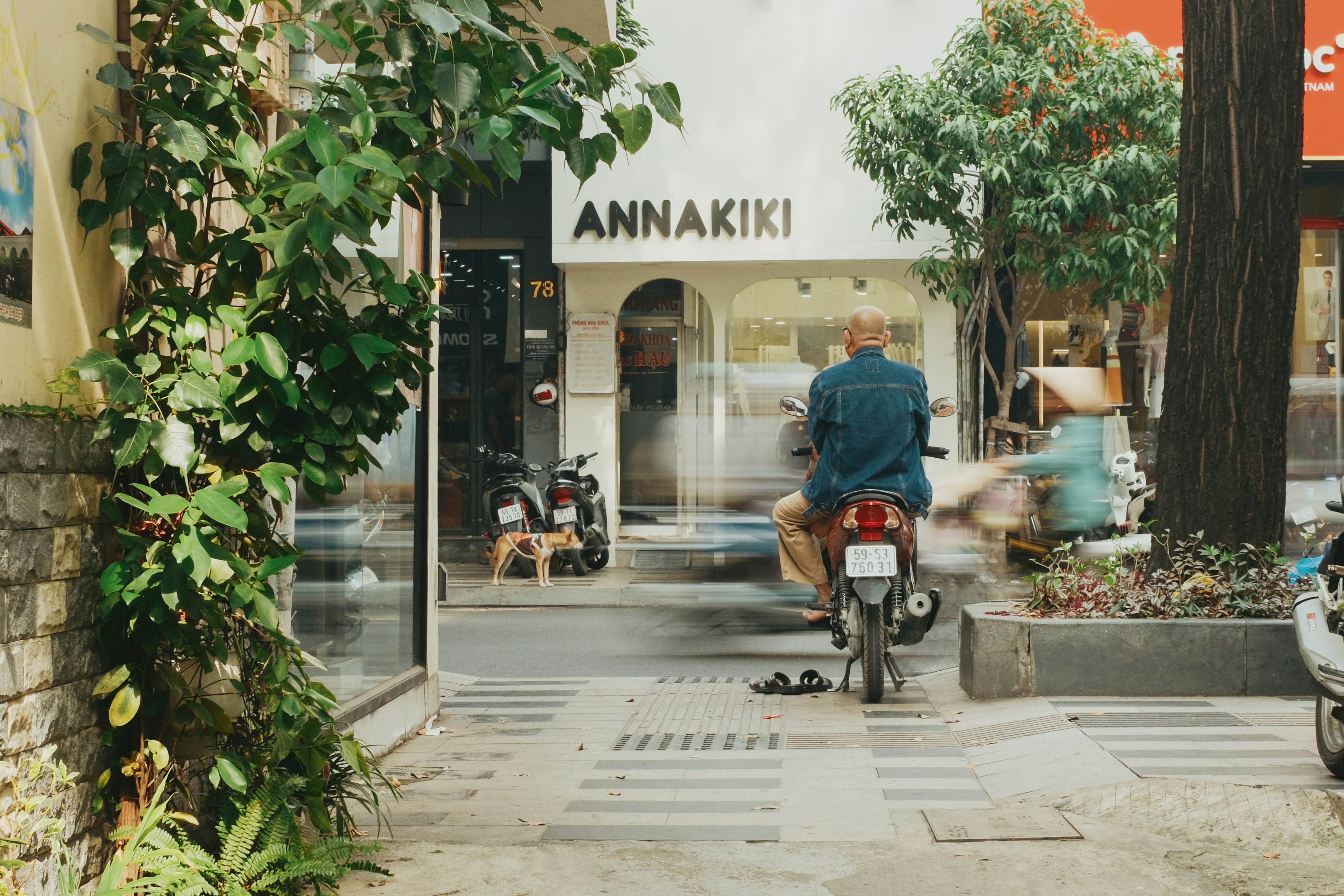 Man rides scooter past storefronts on city street.