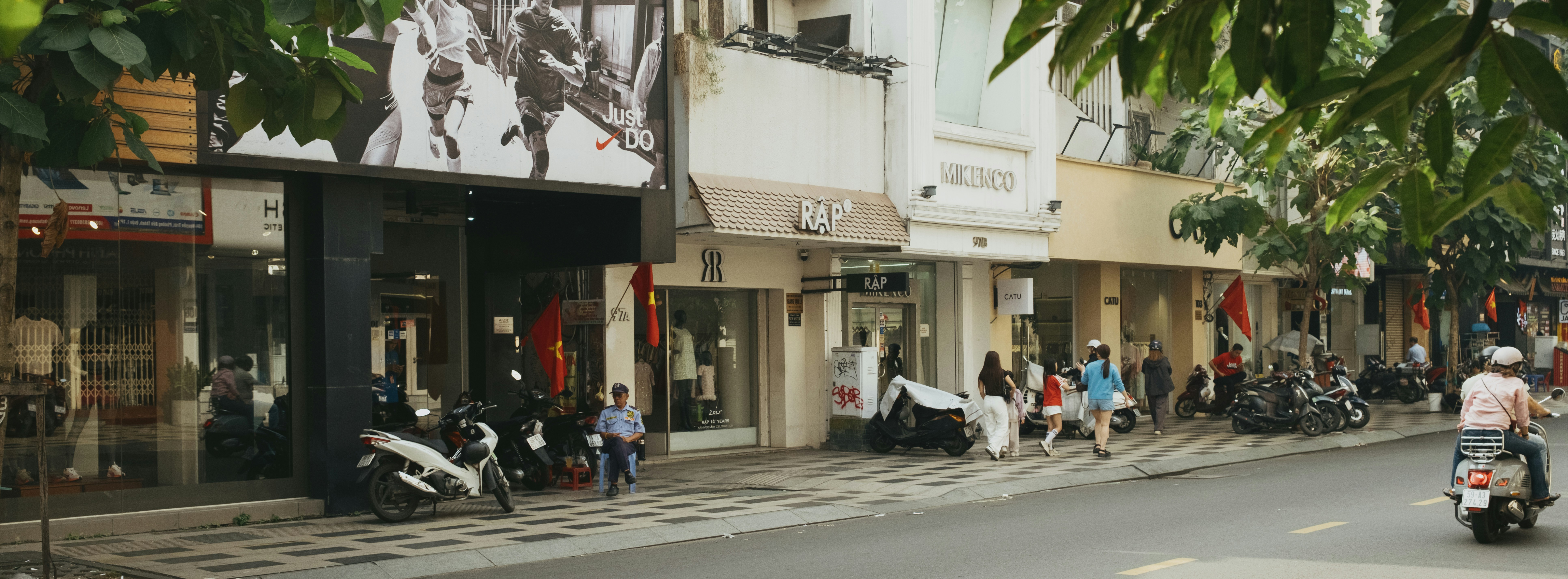 Street scene with shops, motorcycles, and people walking.