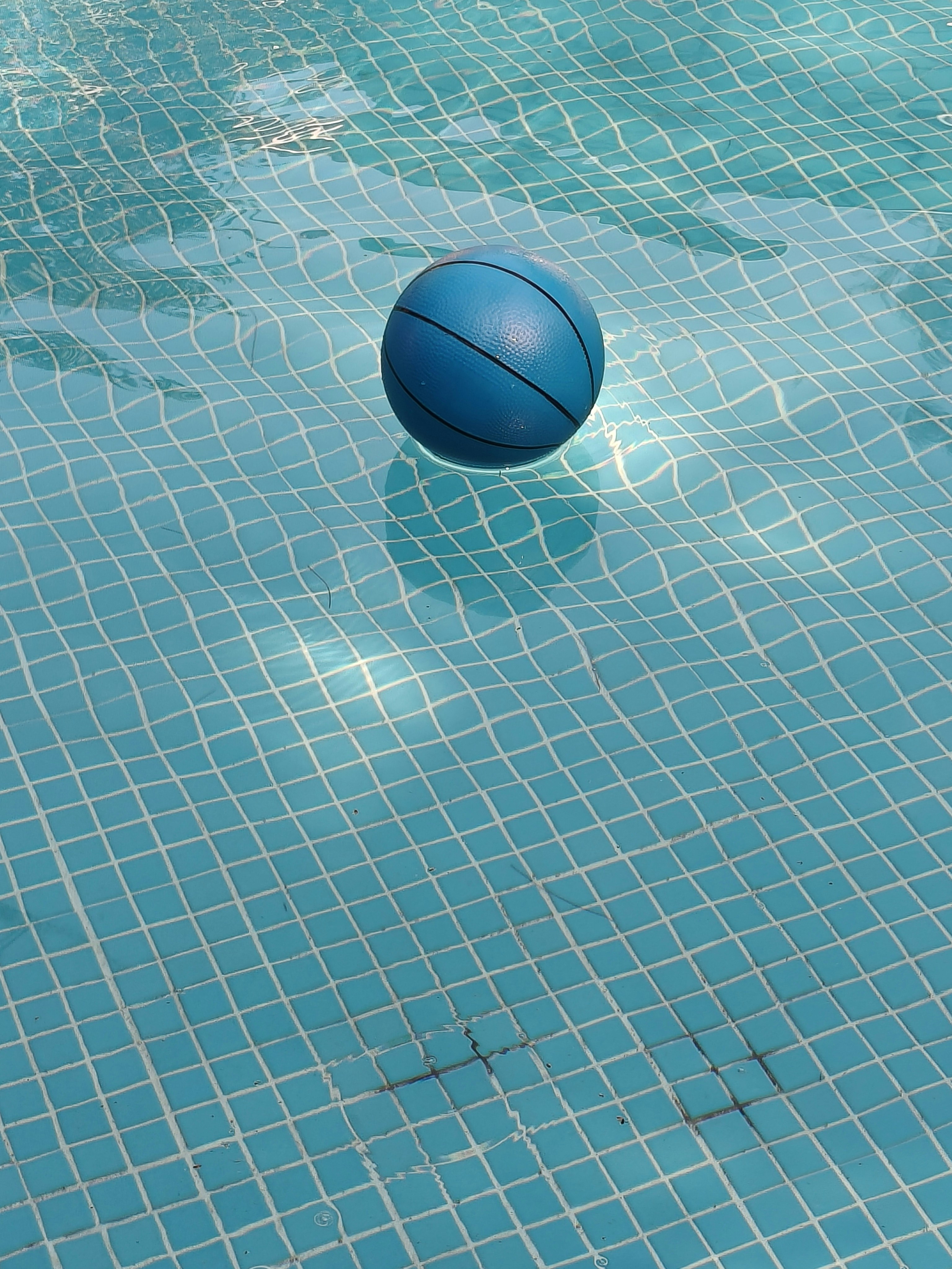 A blue ball floats in a tiled swimming pool.