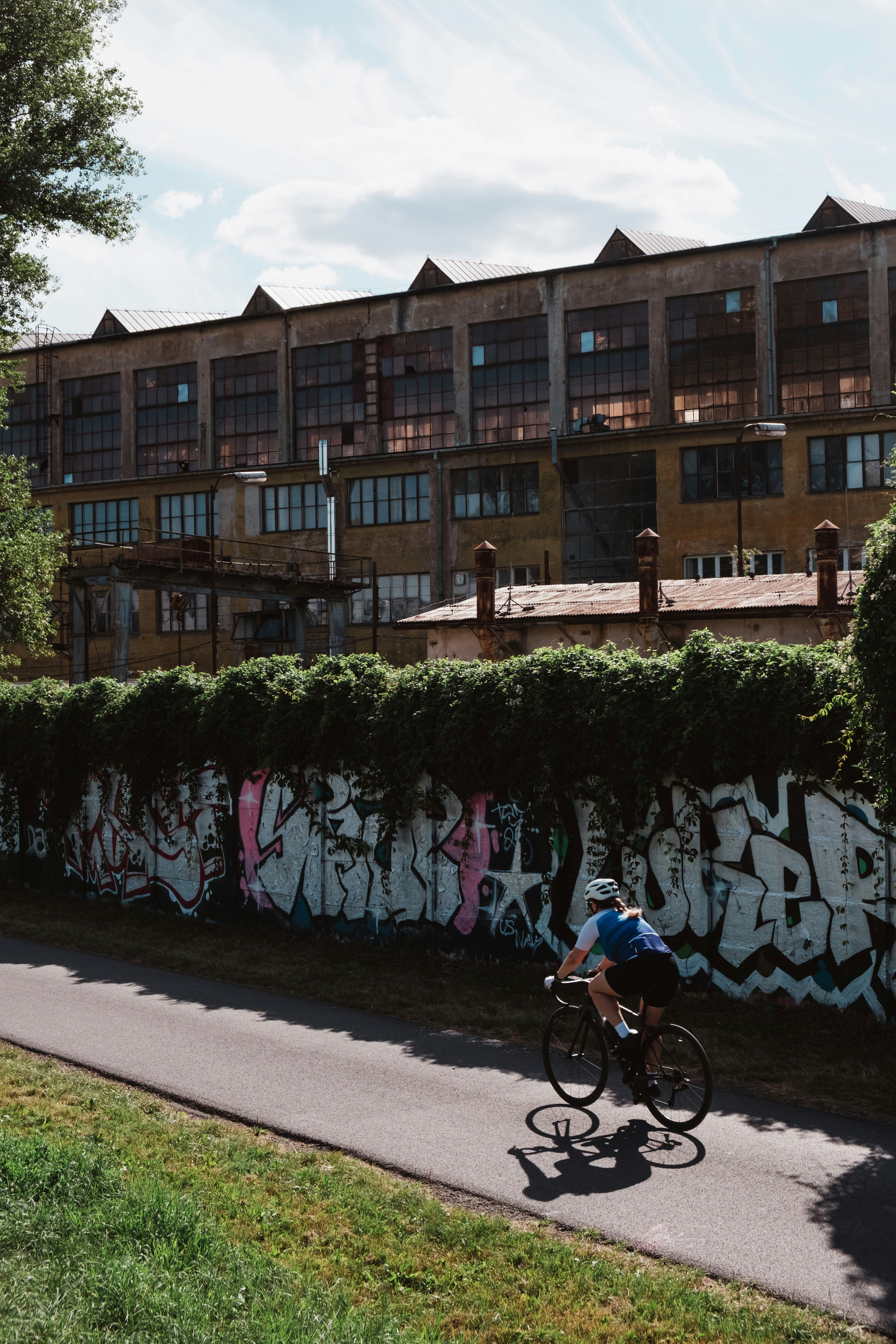 Cyclist rides past graffiti-covered wall near old factory