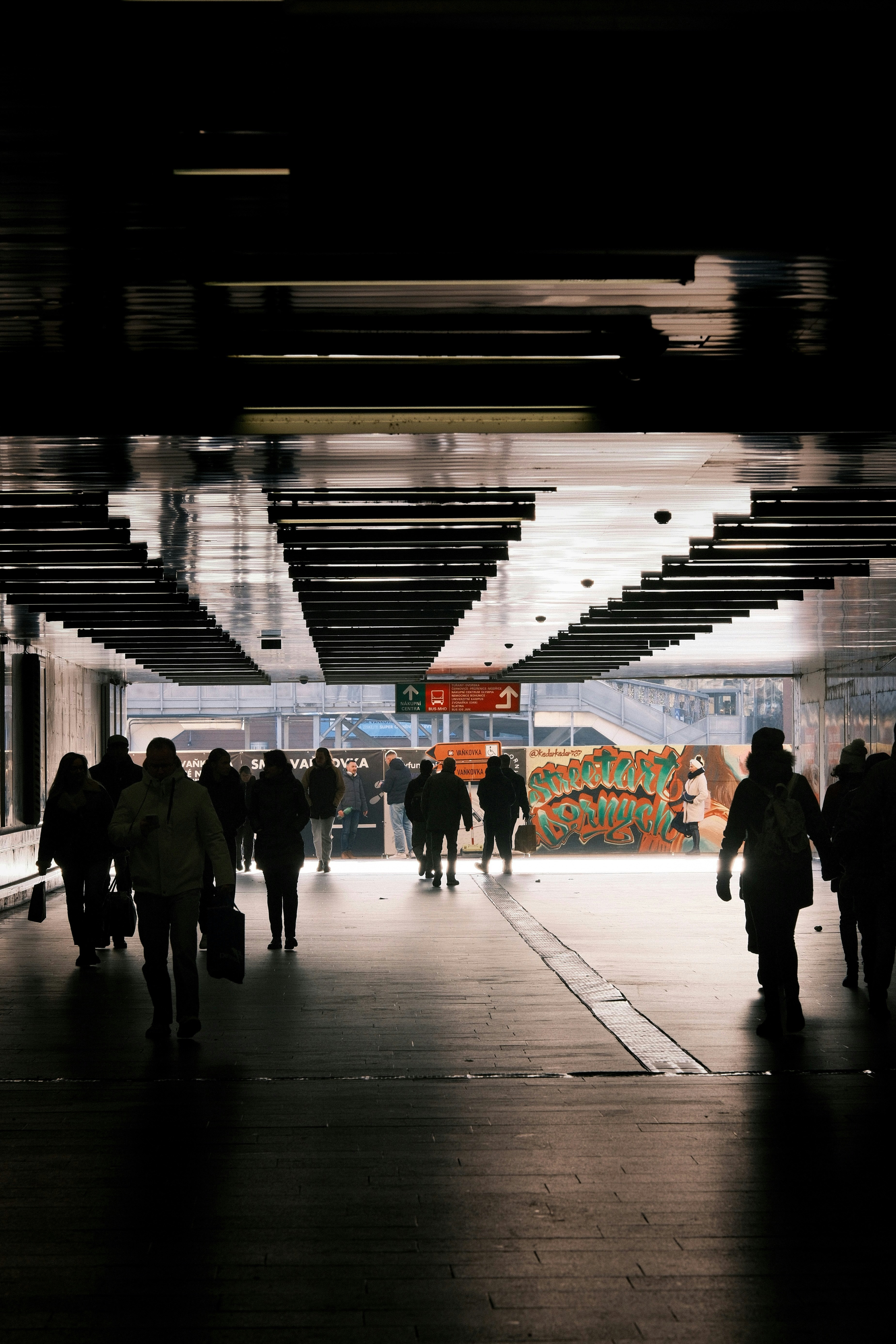 Silhouetted people walking through a brightly lit underpass.