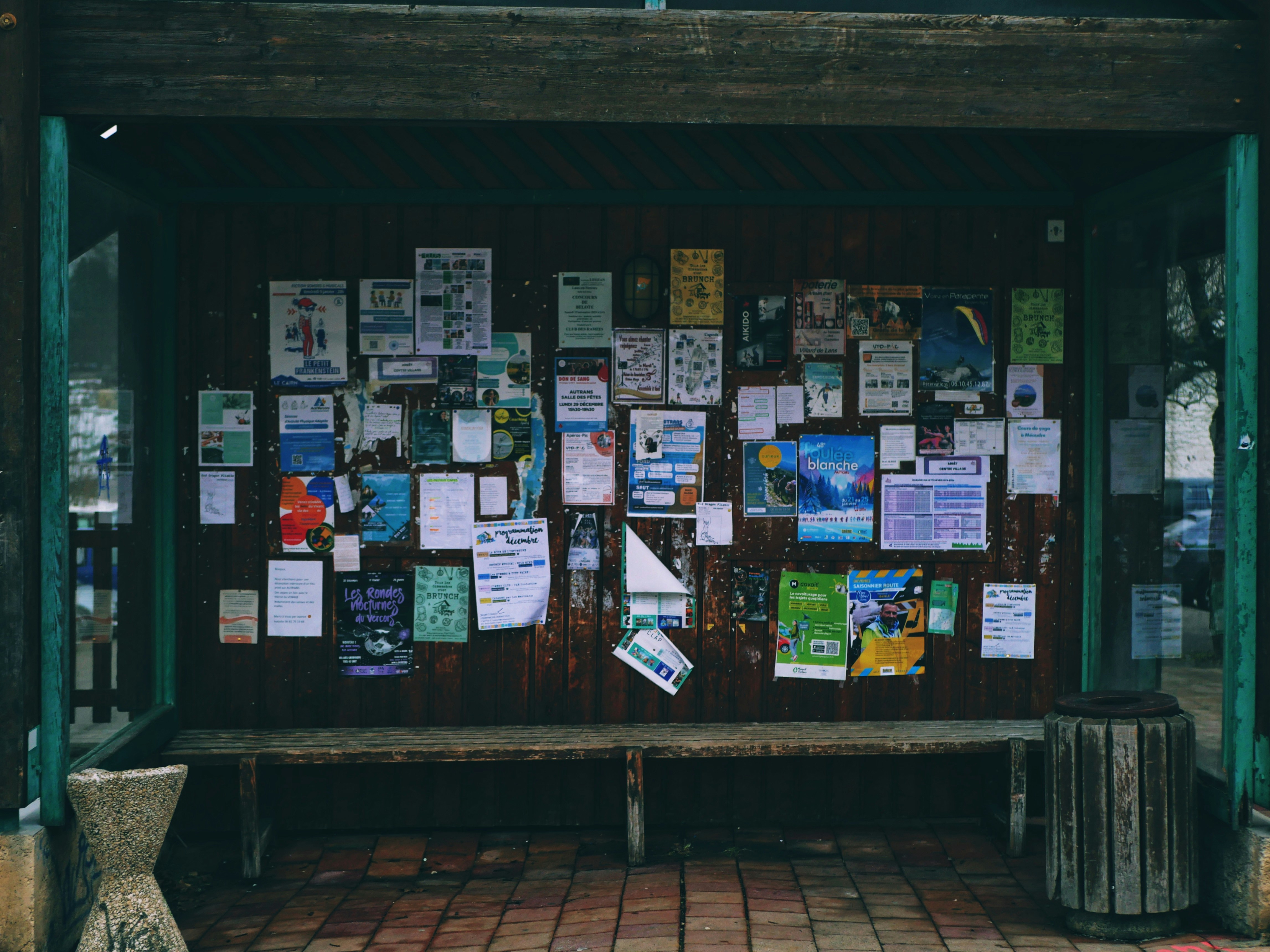 Un tableau d’affichage couvert de flyers avec un banc.