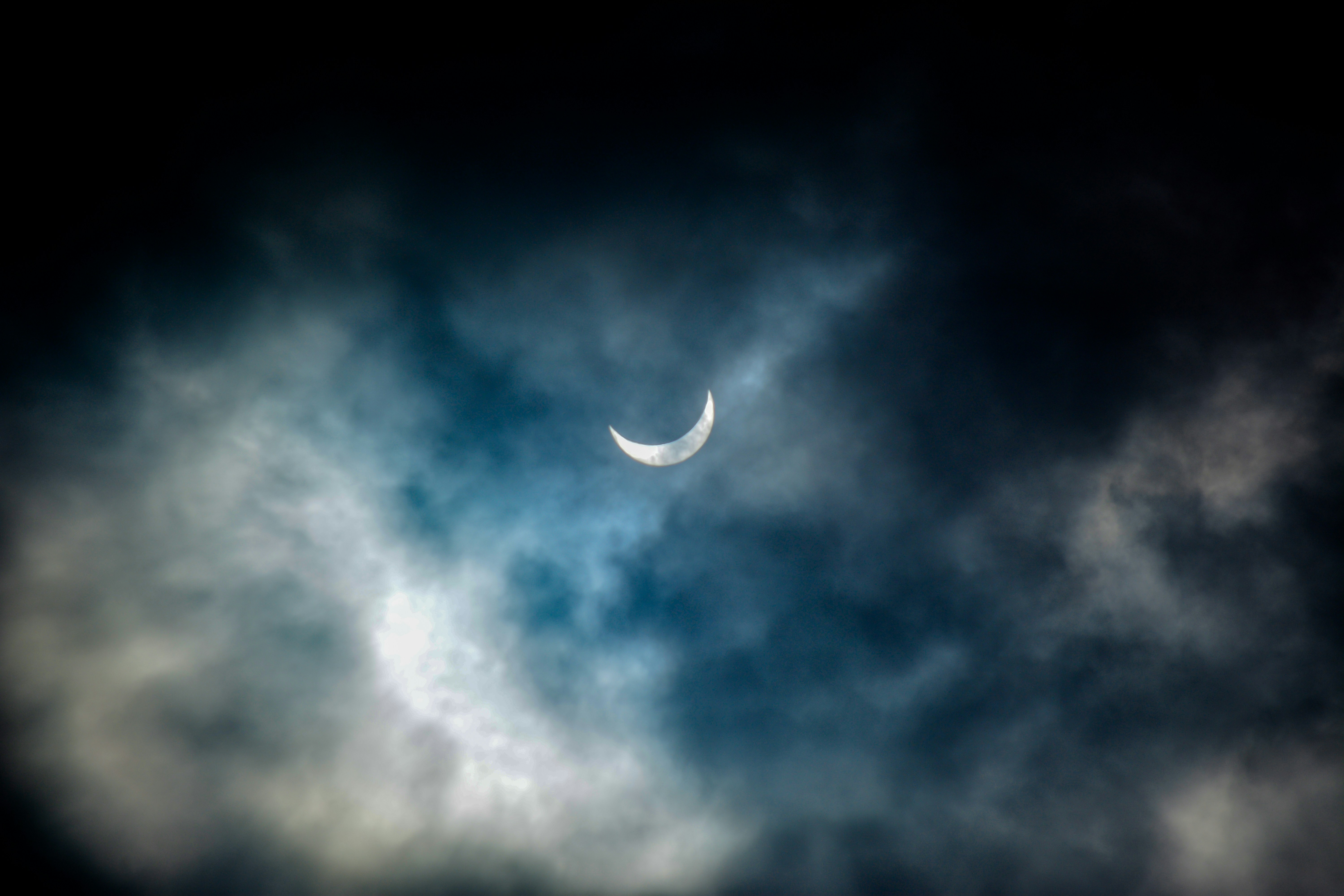 Crescent sun visible through dark stormy clouds.