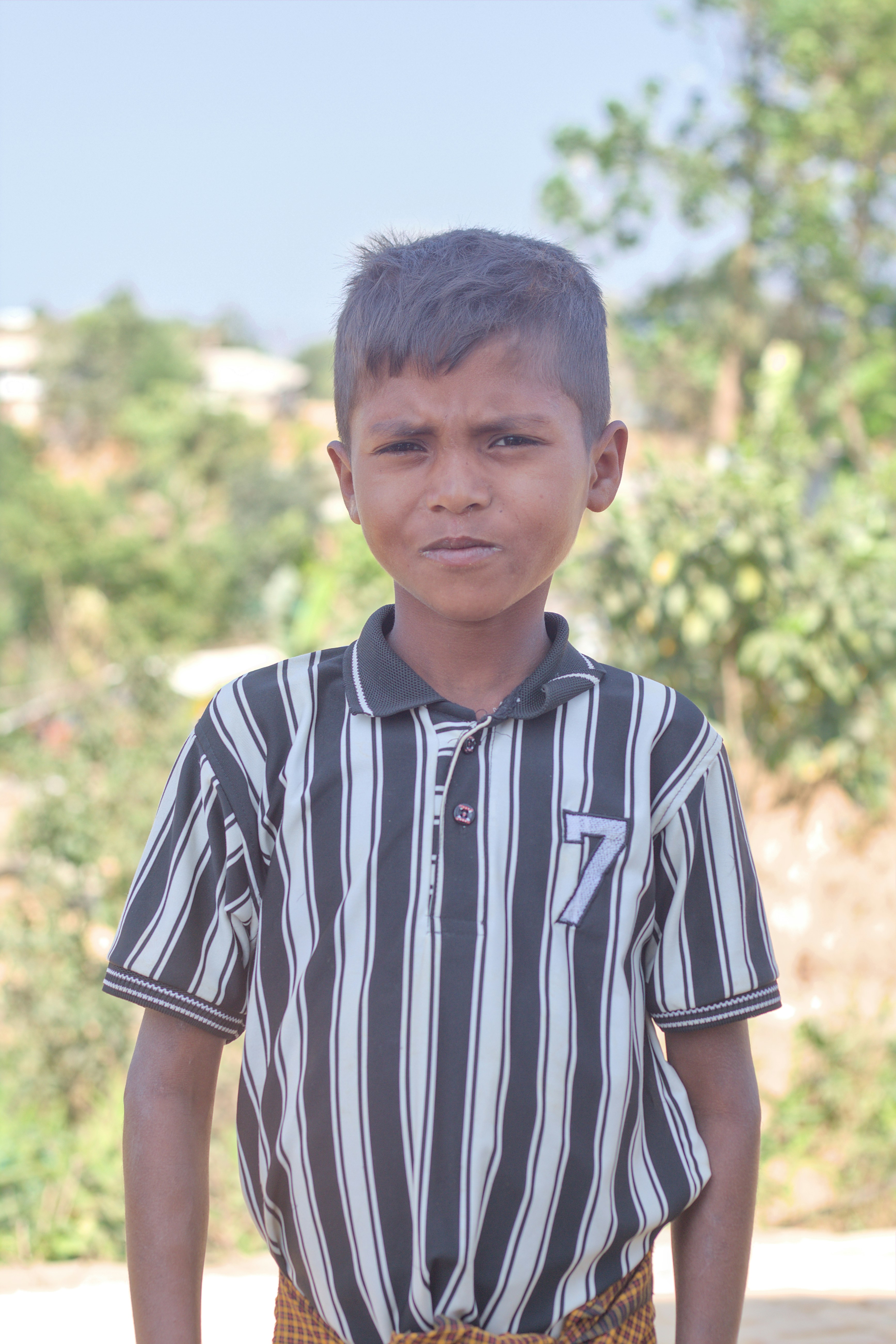 Young boy in striped shirt stands outdoors.