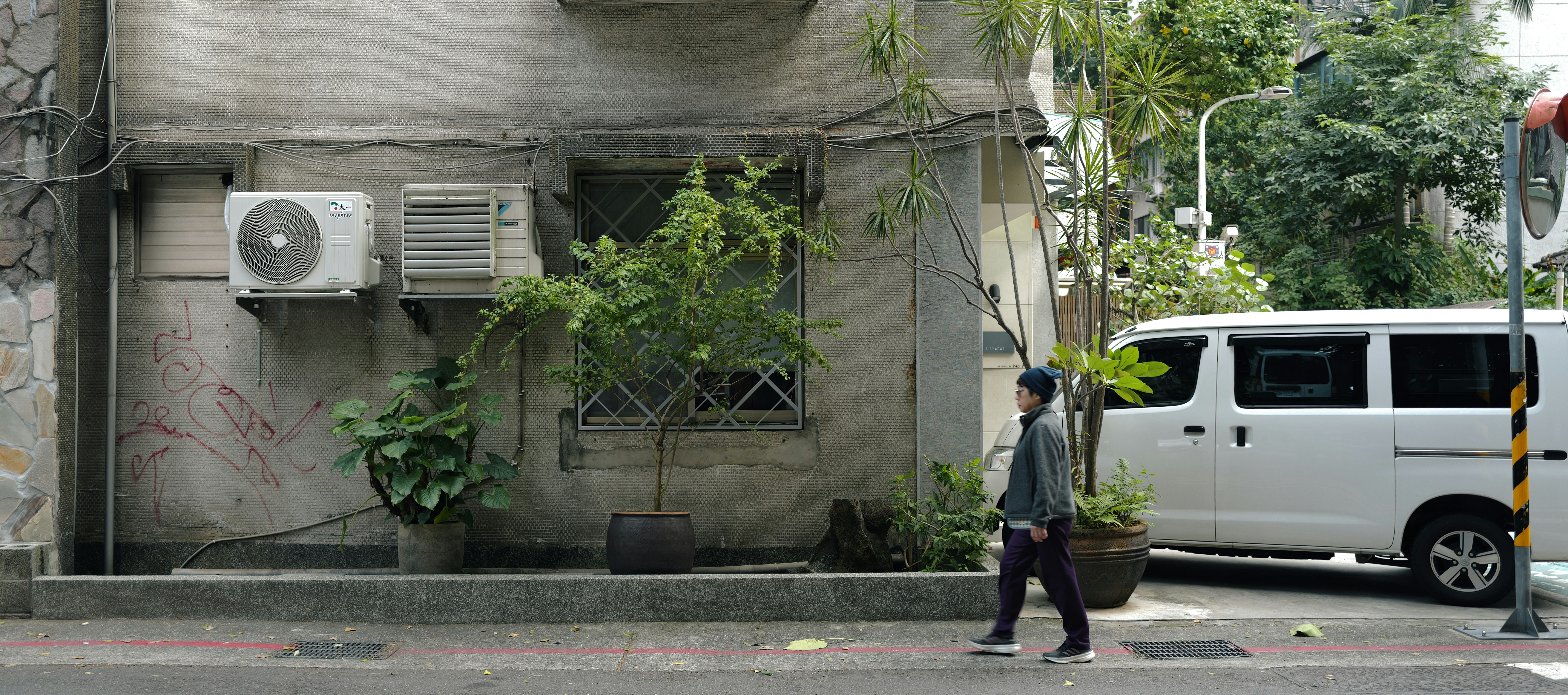 Person walks past building with air conditioners and van.