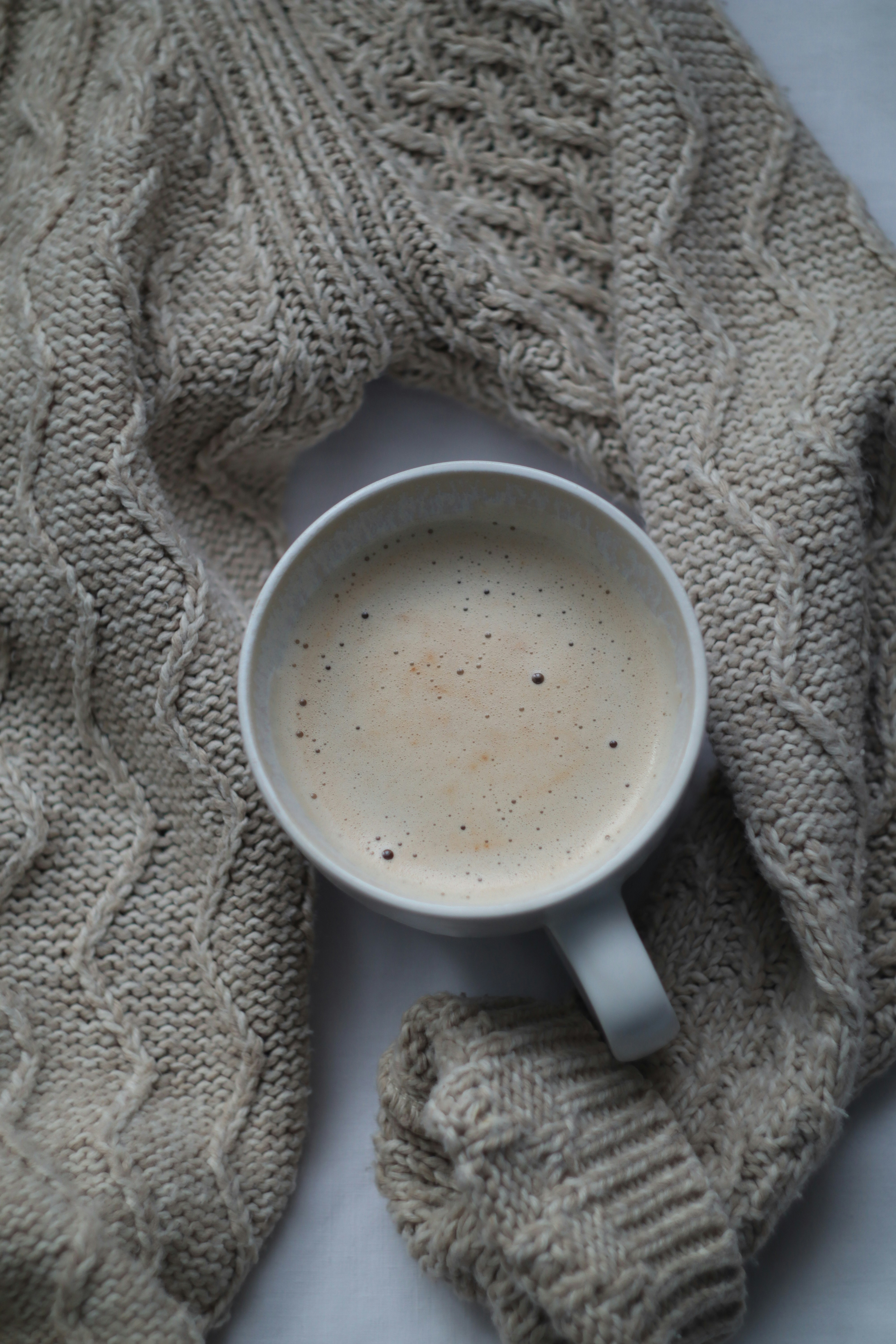 Eine Tasse Kaffee steht auf einem gestrickten Pullover.