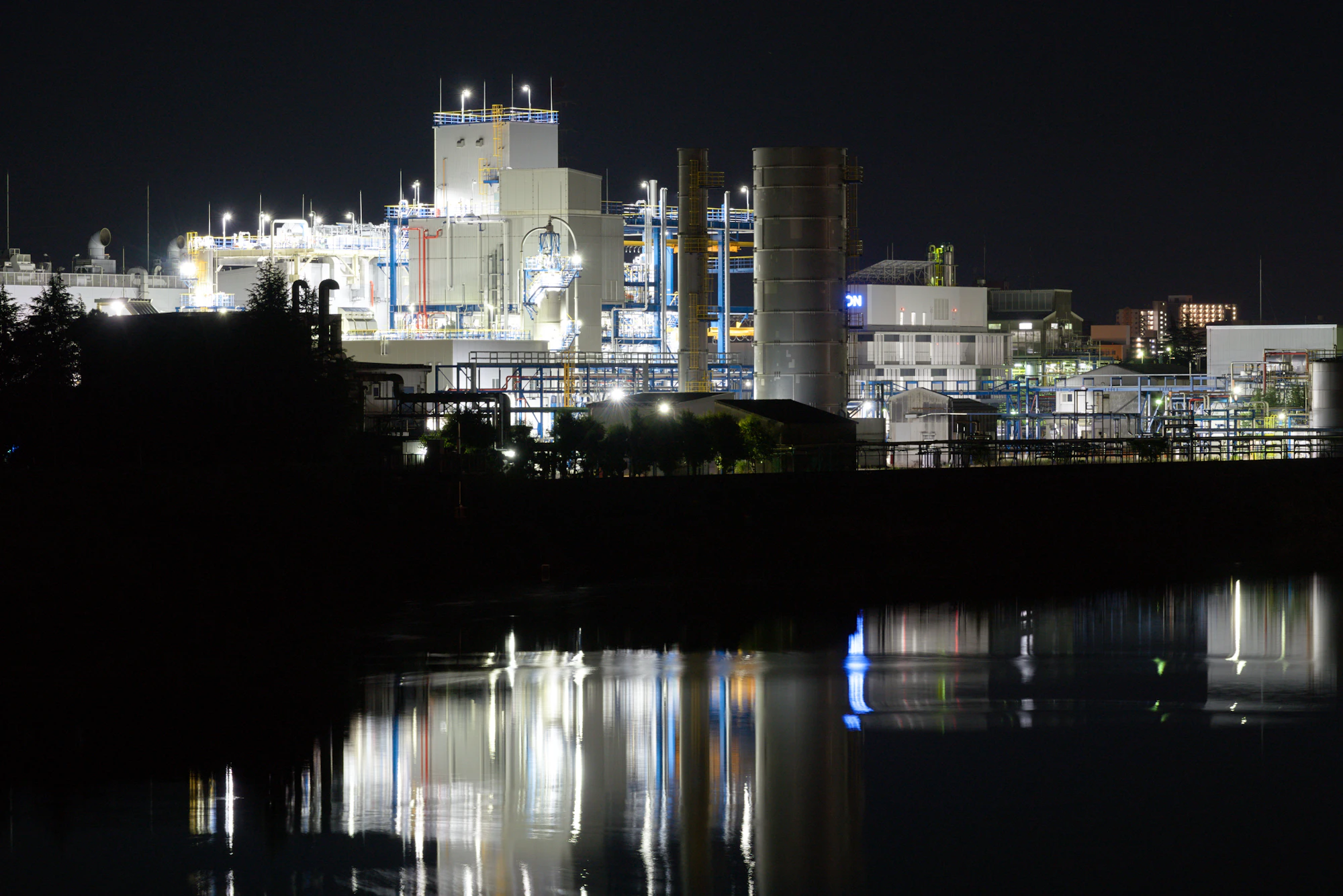 Industrial processing facility illuminated at night, reflected in adjacent water