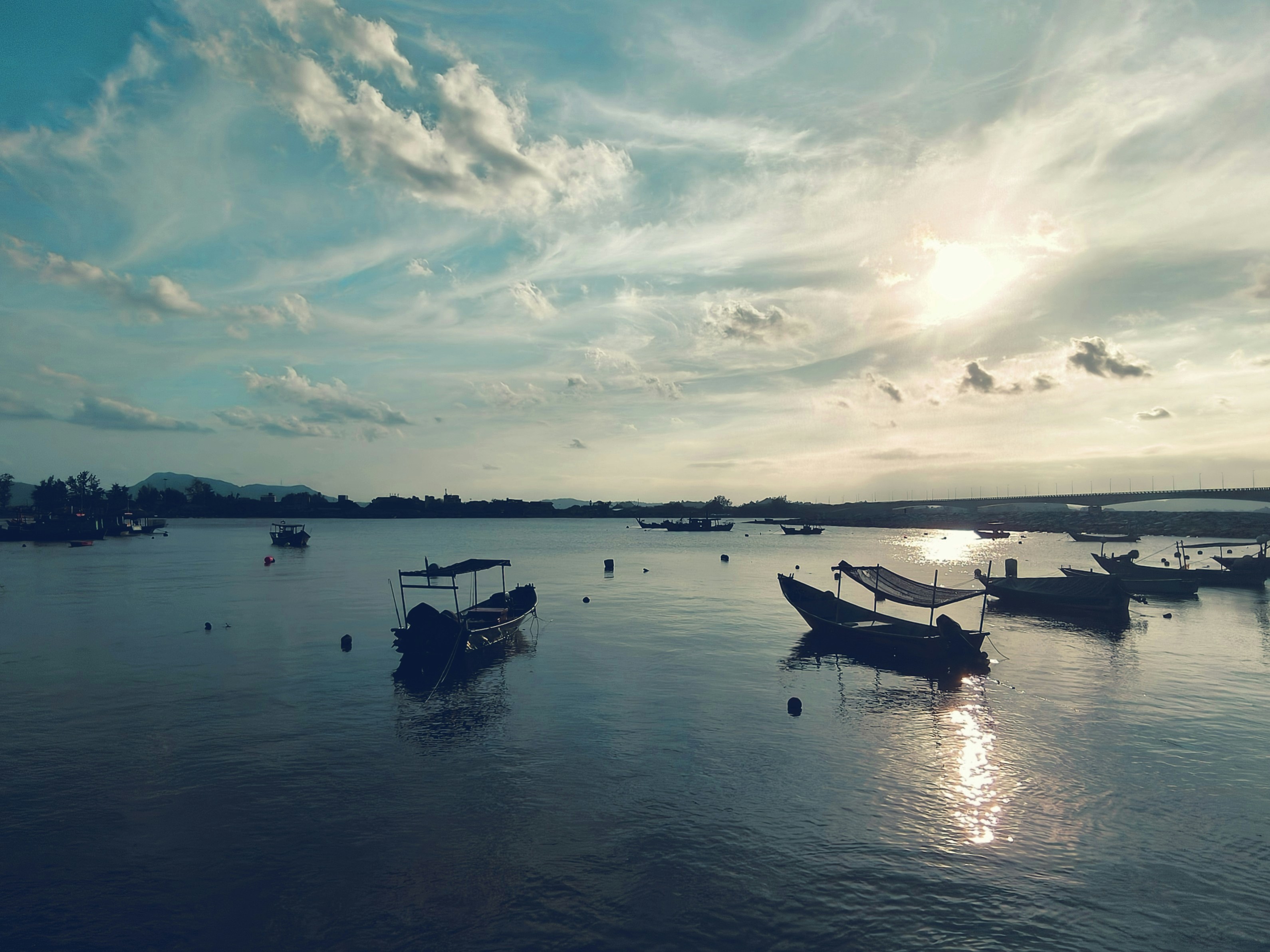 Fishing boats float on calm water under a cloudy sky.