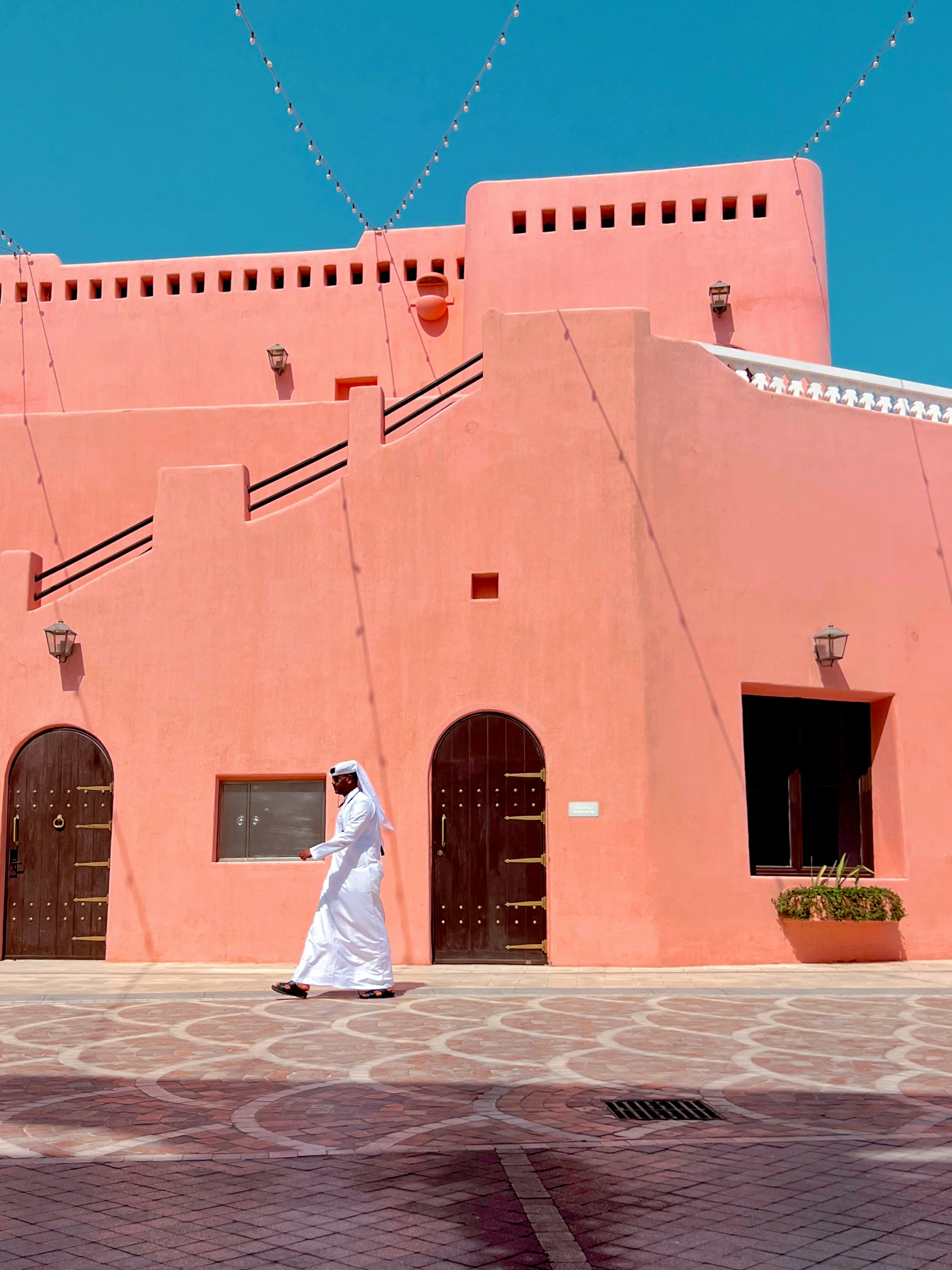 Man in traditional white clothing walks past pink building.