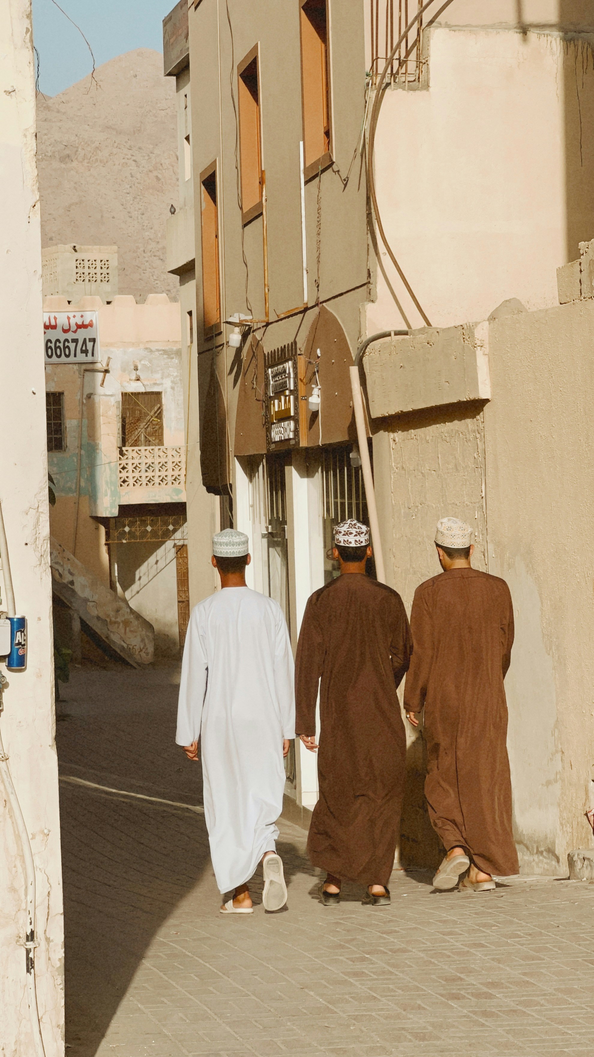 Three men walk down a narrow street.