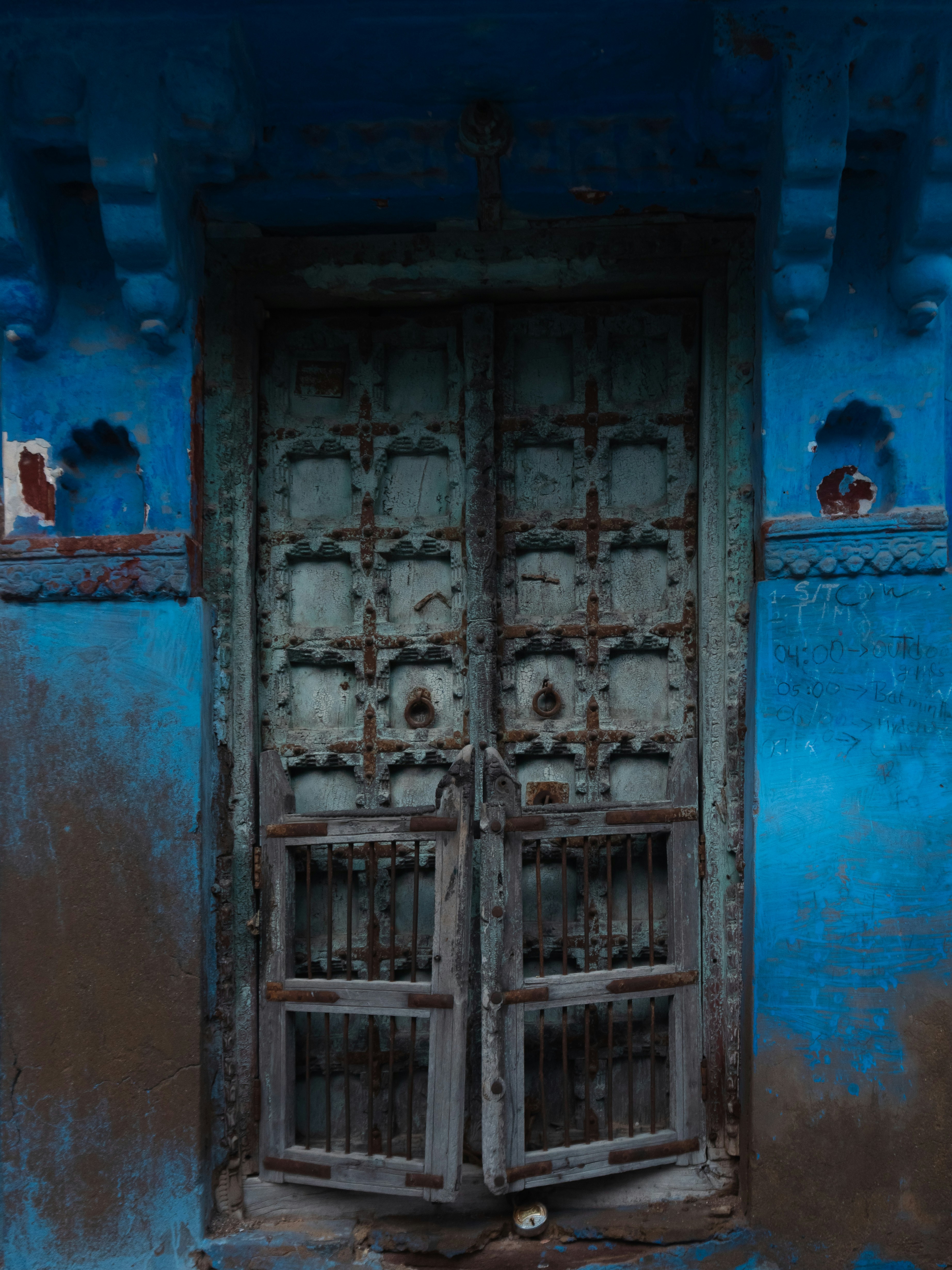 An old weathered blue door in a vibrant blue wall.