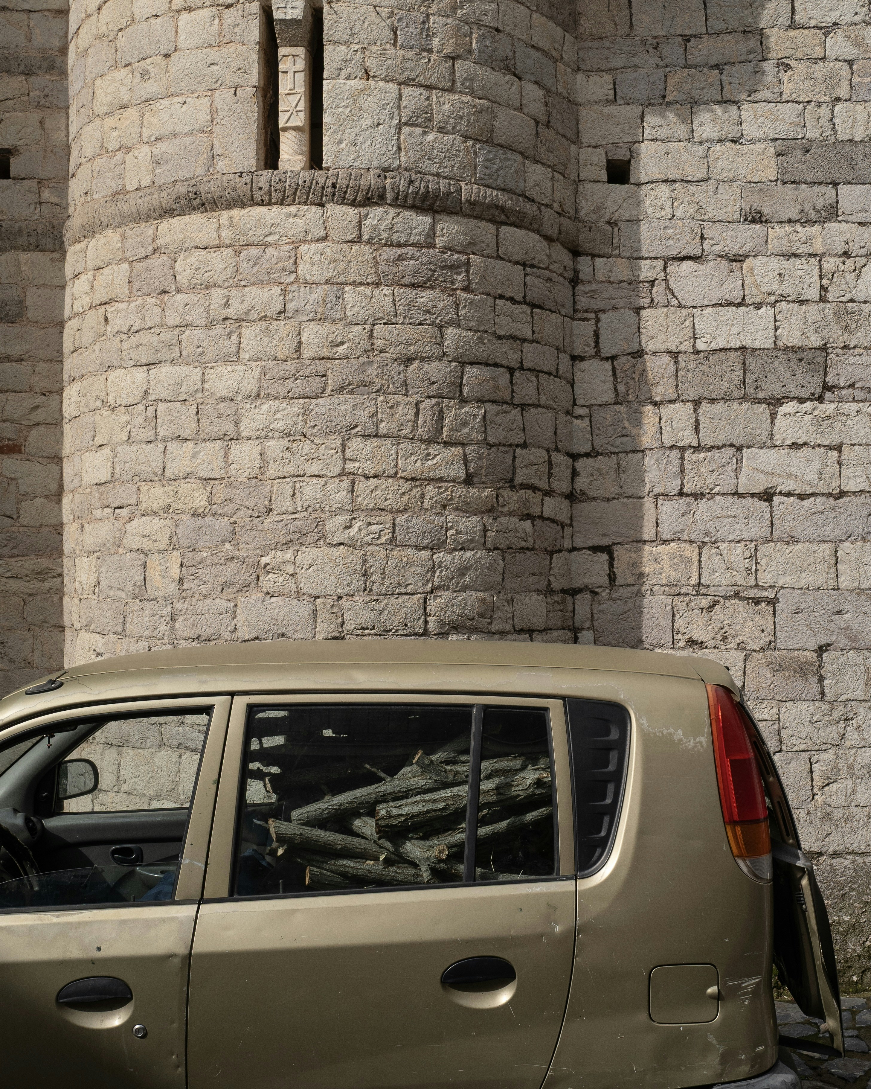 Car filled with logs parked by stone building