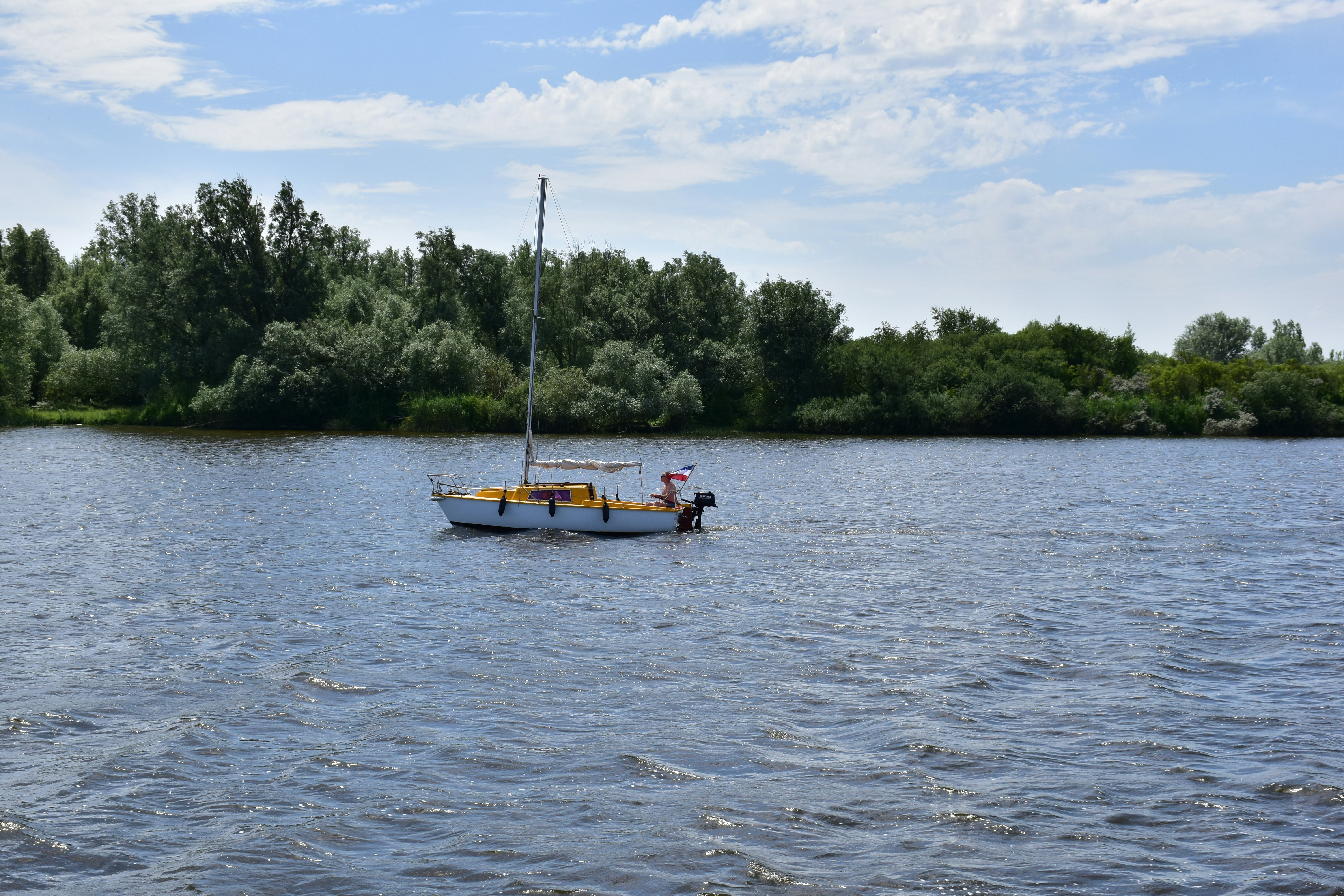 Sailboat on a calm blue lake with green trees.