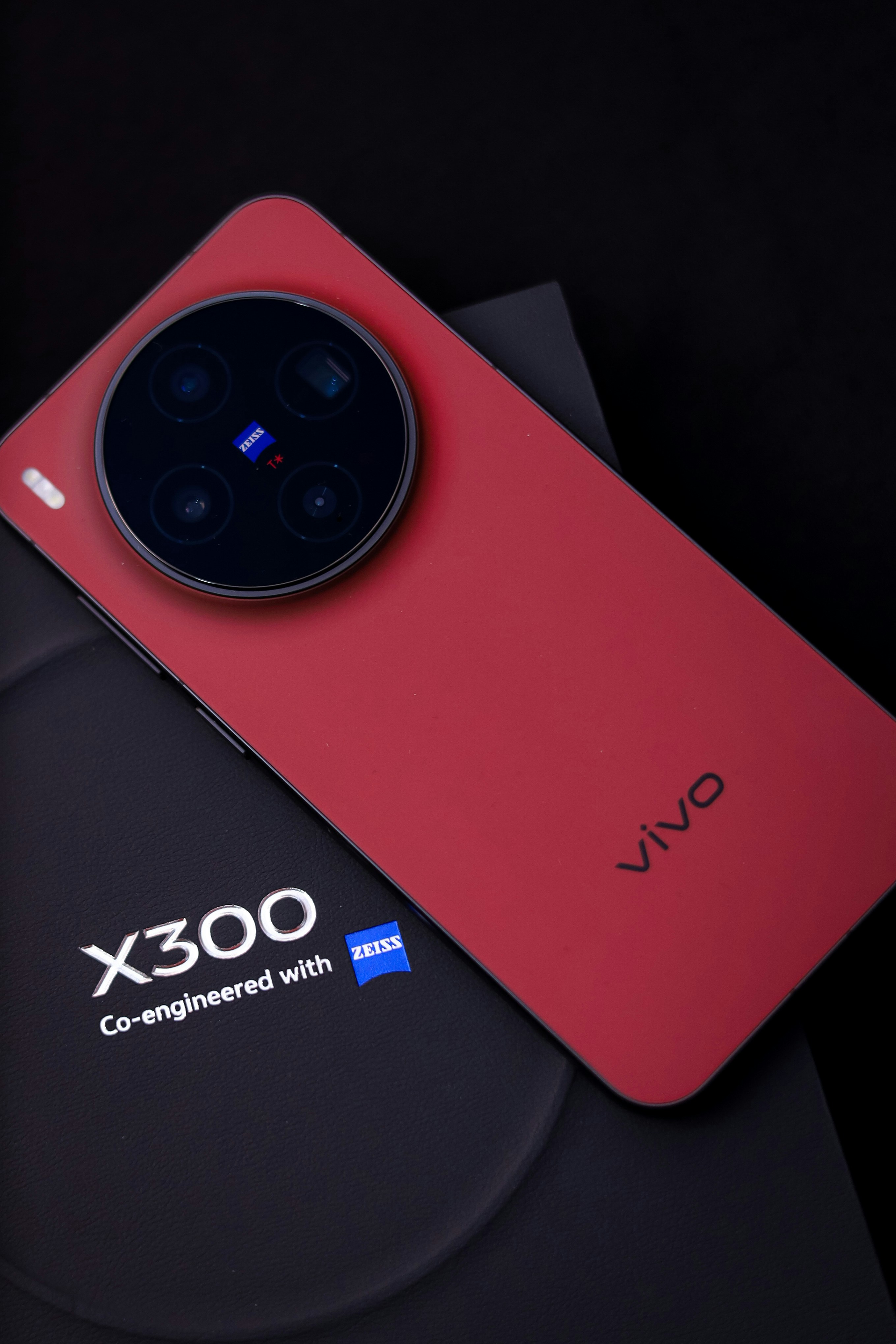 Red smartphone with circular camera module and zeiss logo.