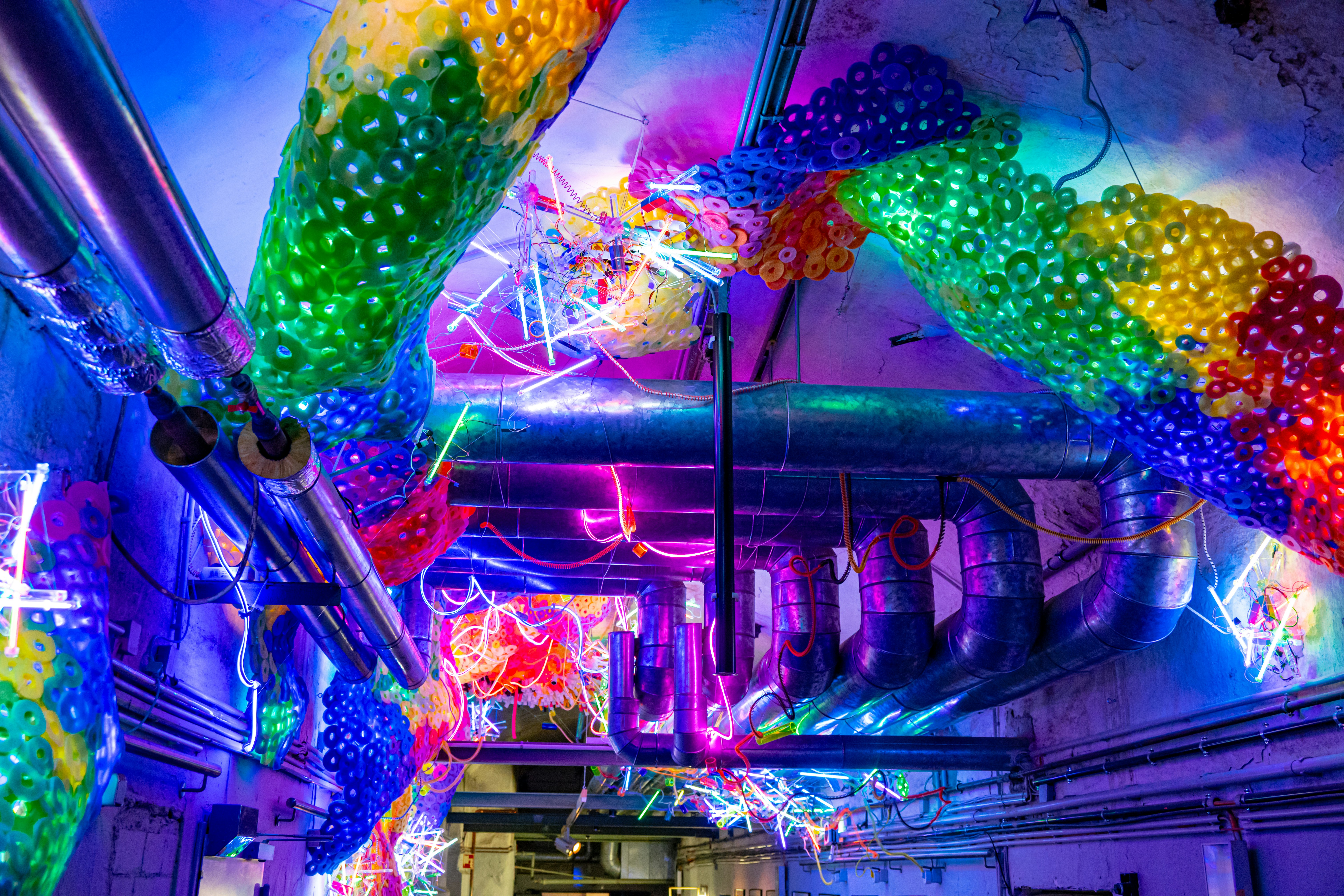 Colorful lights illuminate industrial pipes and decorations.