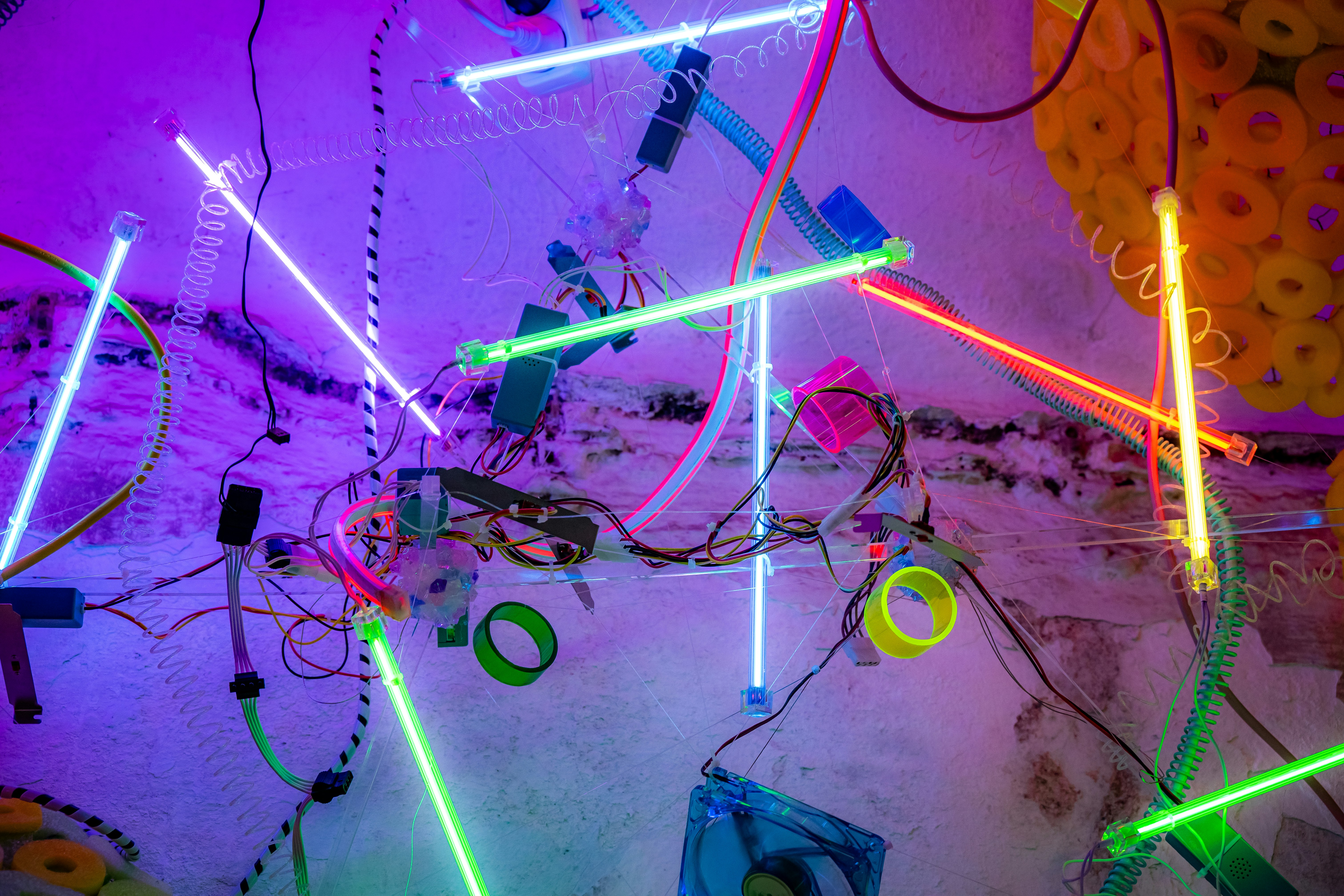 Neon lights illuminate a cluttered, abstract art installation.