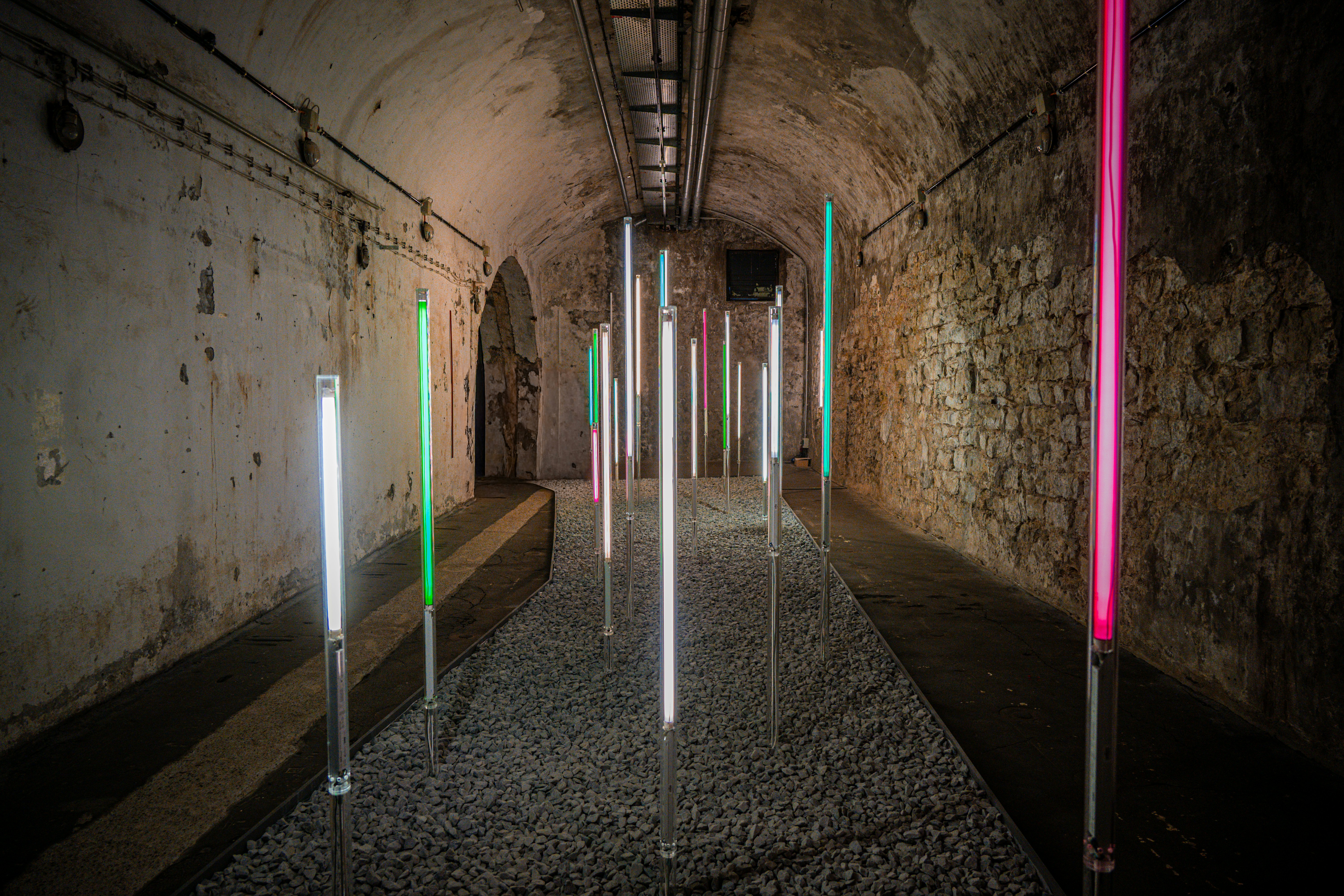 Colored lights illuminate a stone tunnel with gravel floor.