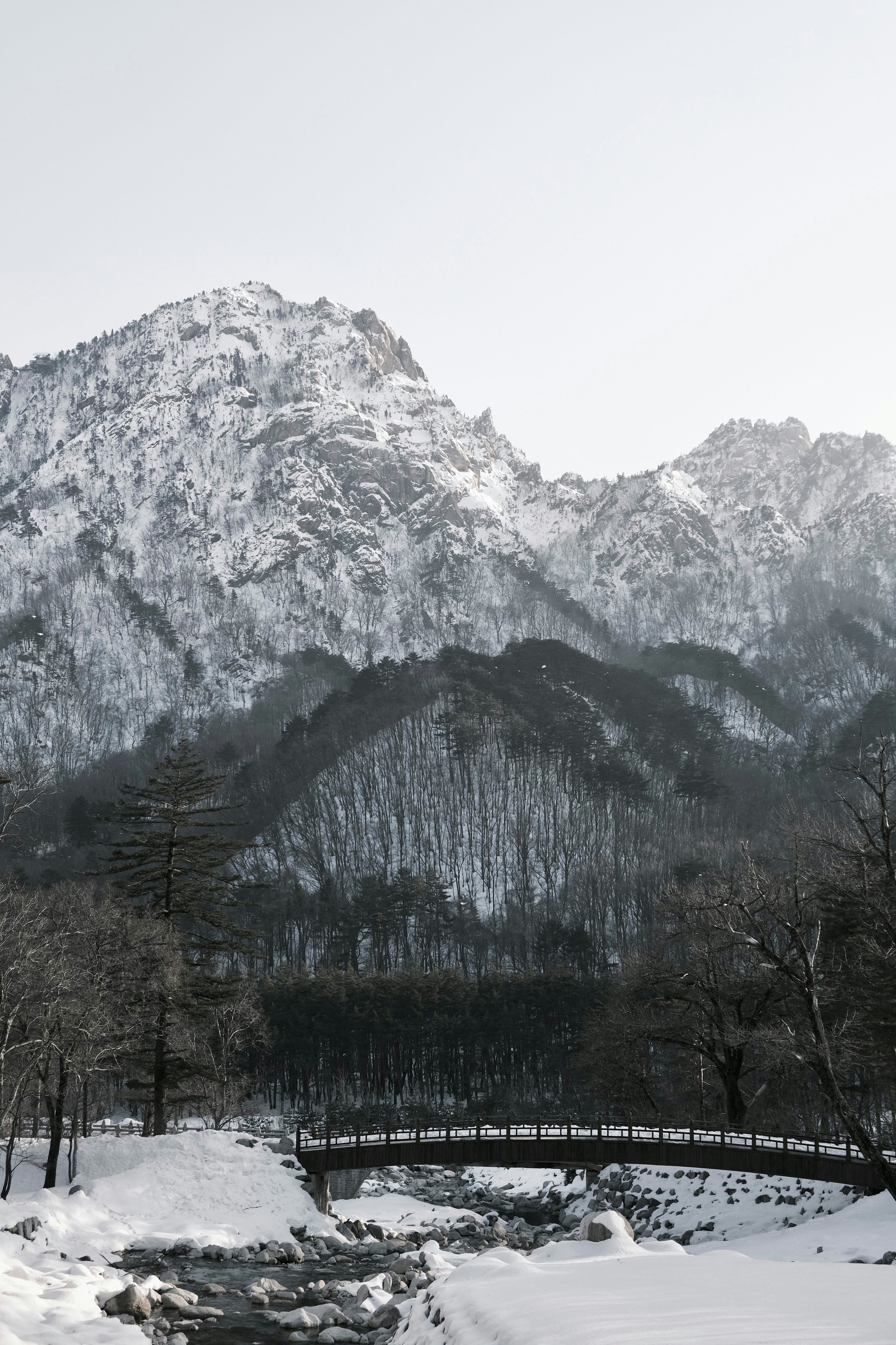 Snow-covered mountains with a bridge over a stream.
