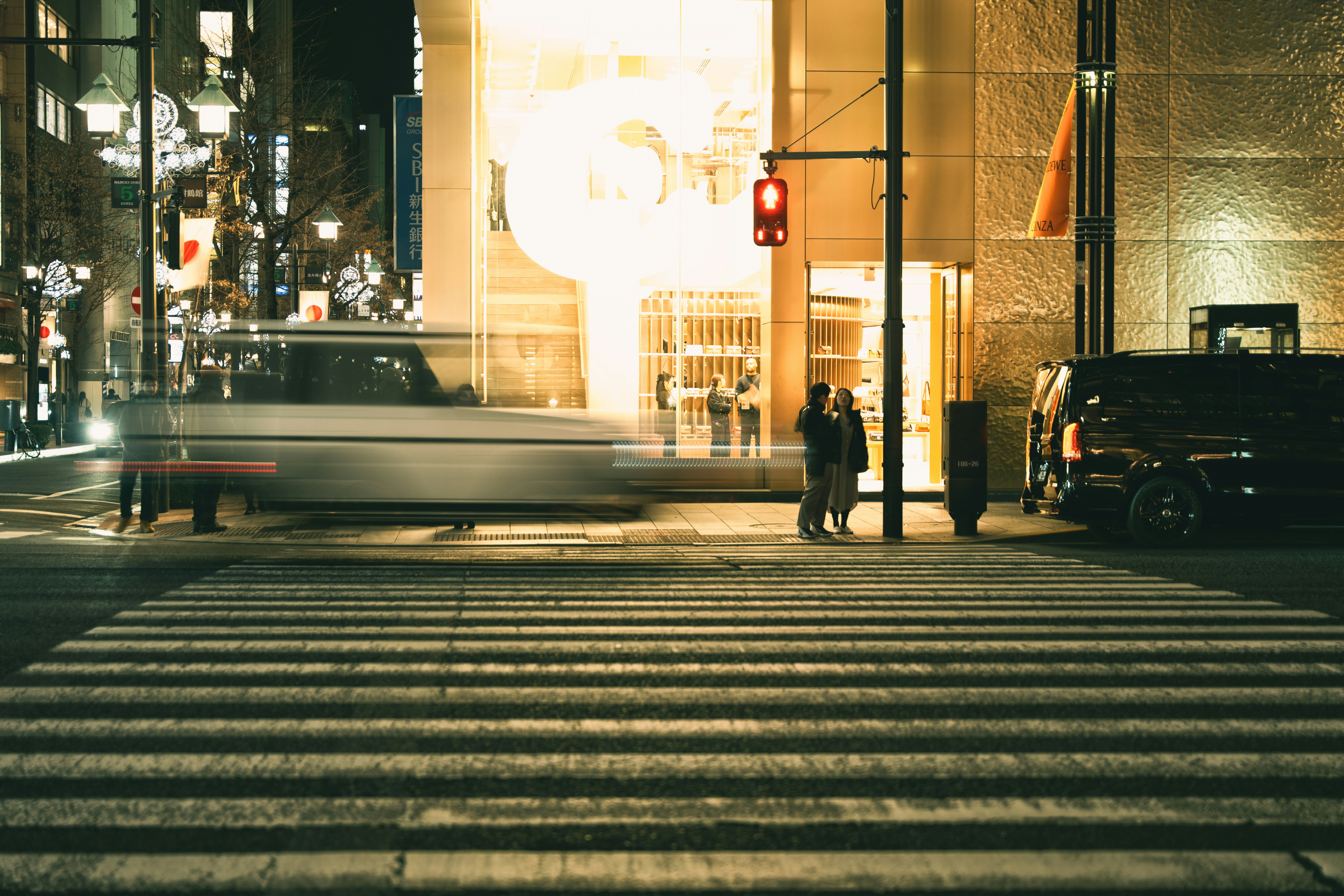 City street at night with blurred car and people.