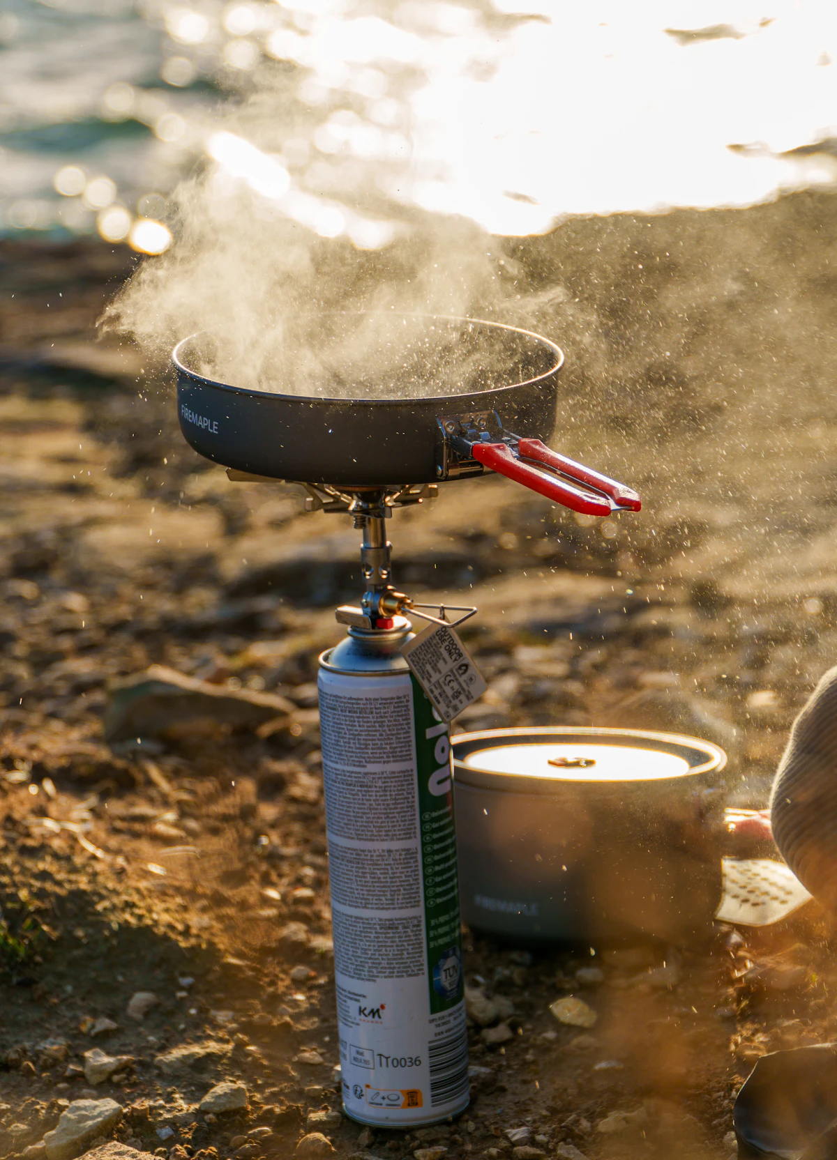 Backpacking canister stove with steaming pot at riverside camp