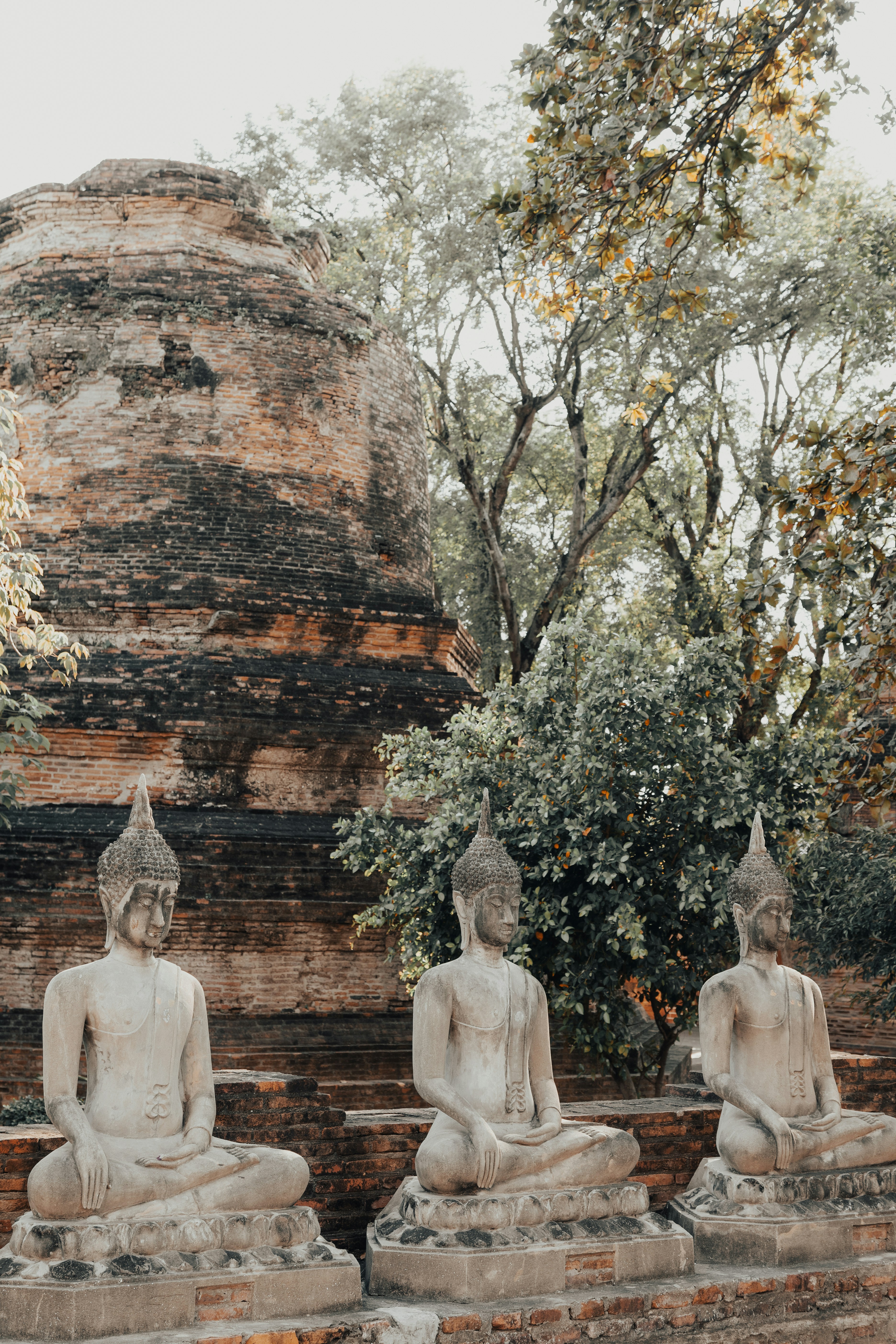 Three ancient buddha statues in front of brick ruins.