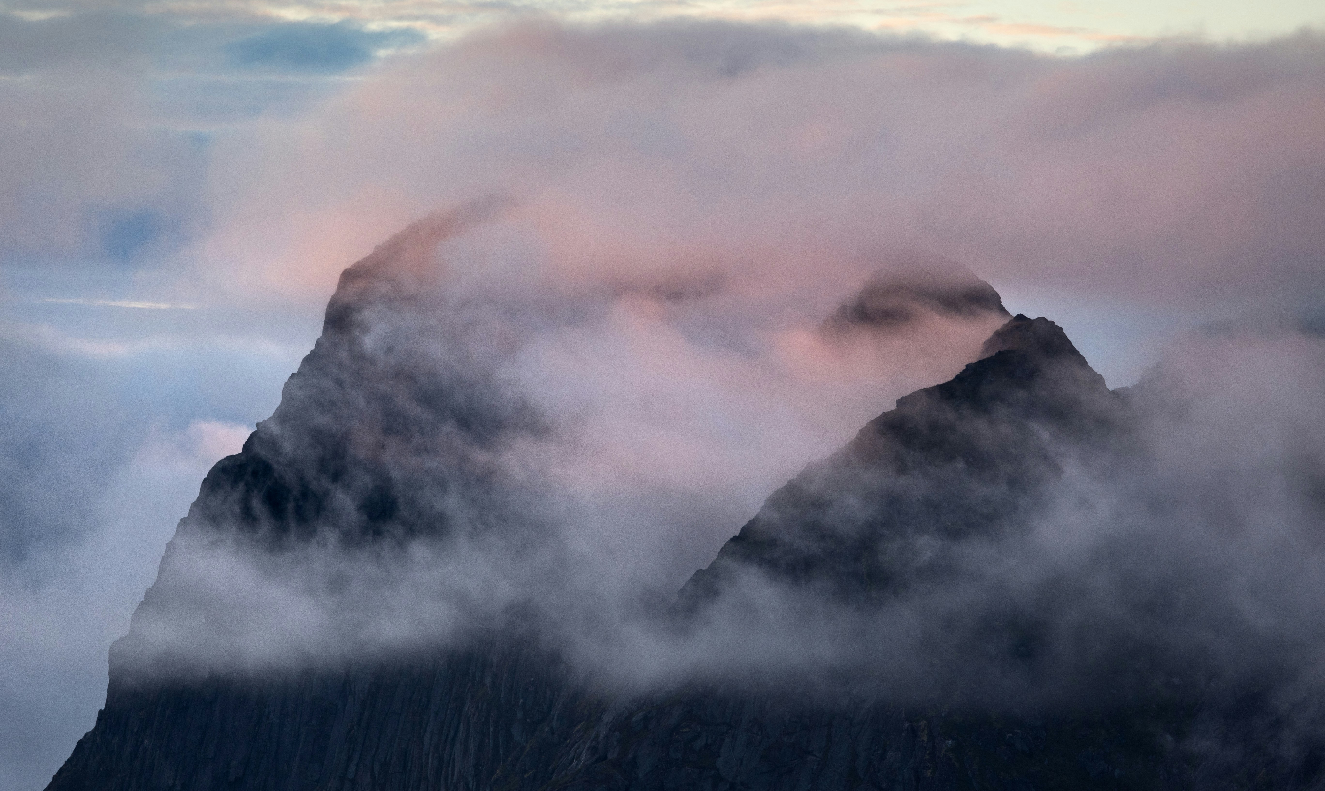 Misty mountain peaks at dawn with soft pink light.