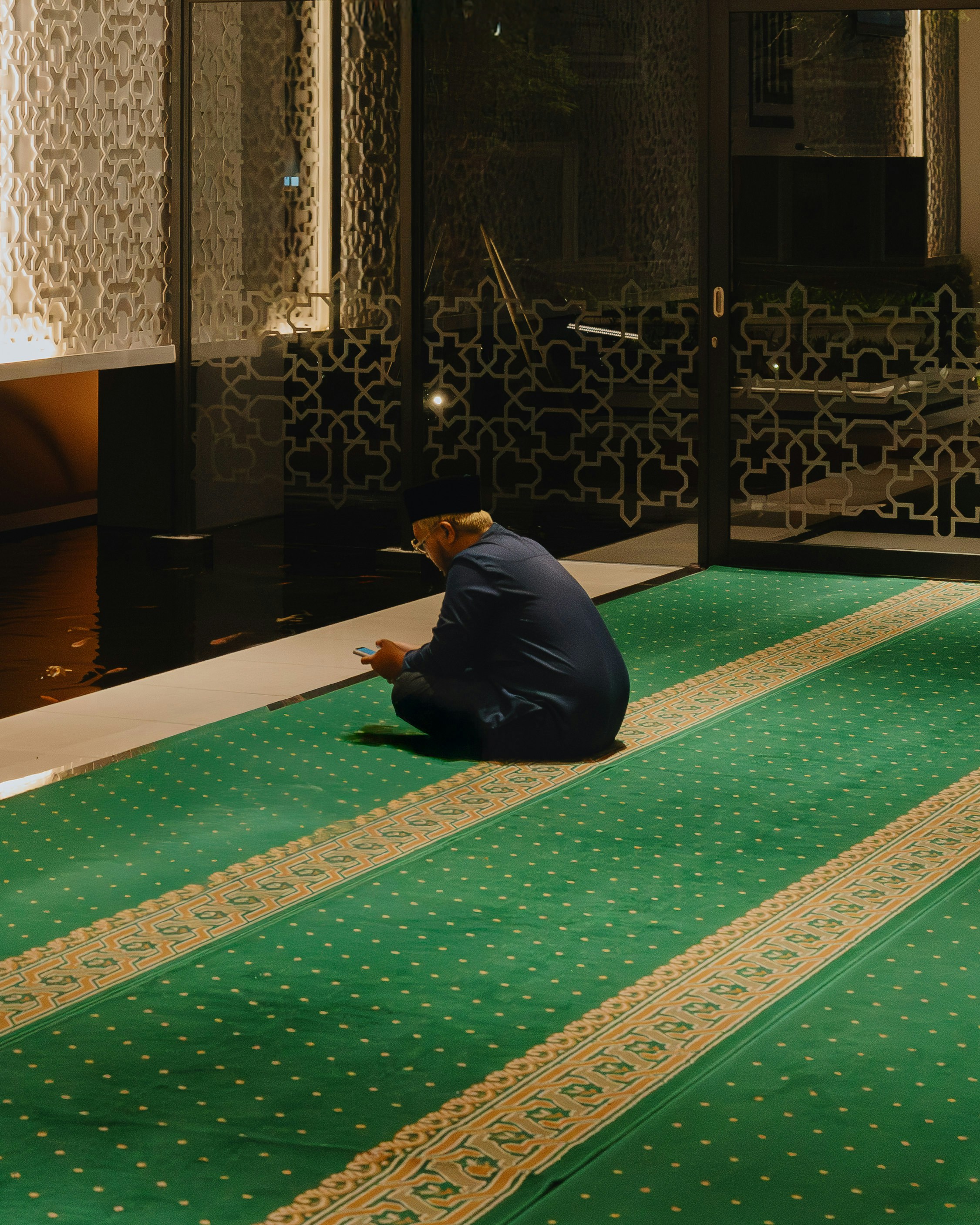 Man praying on a green carpet in a mosque