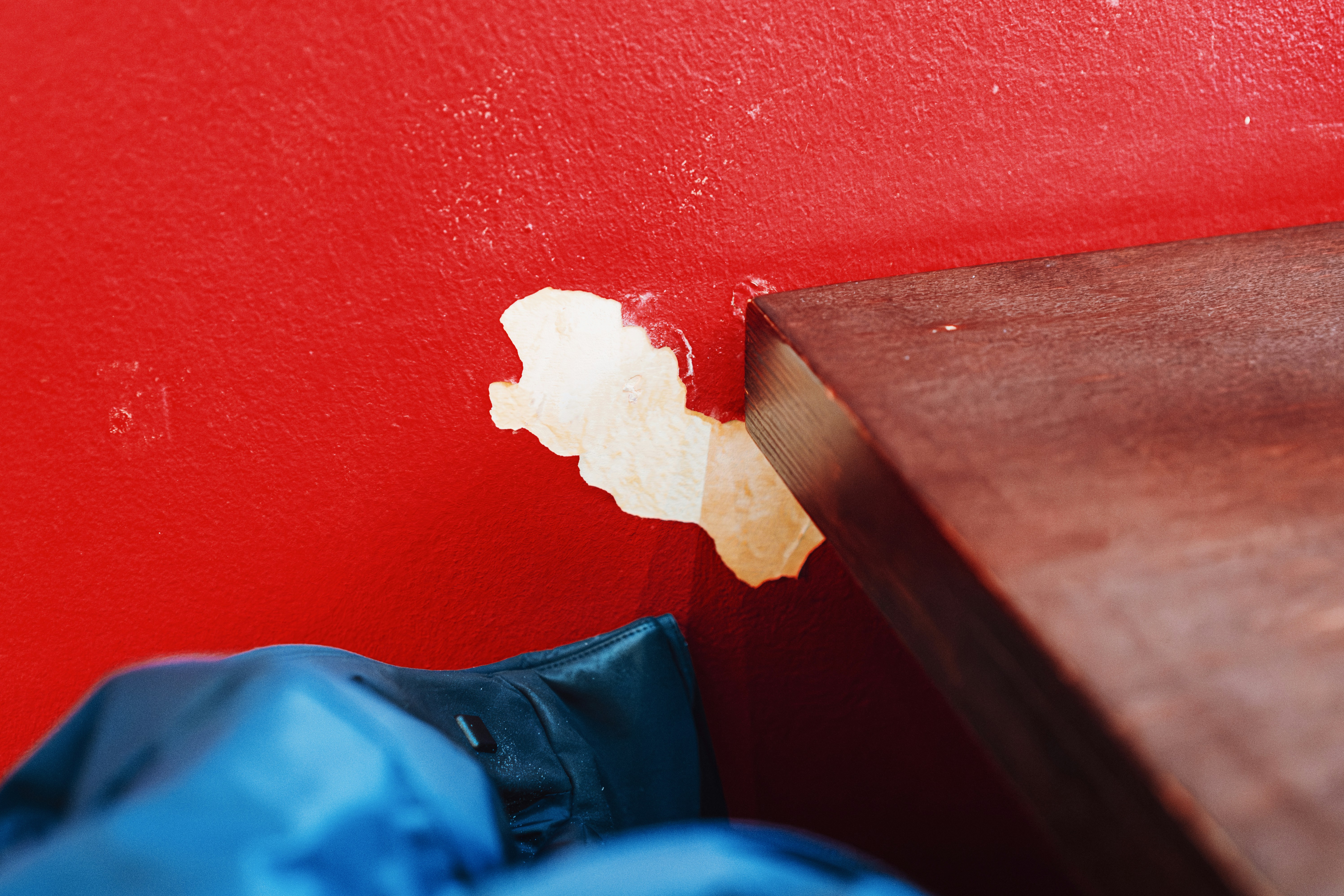 Peeling red paint on a wall next to wood.