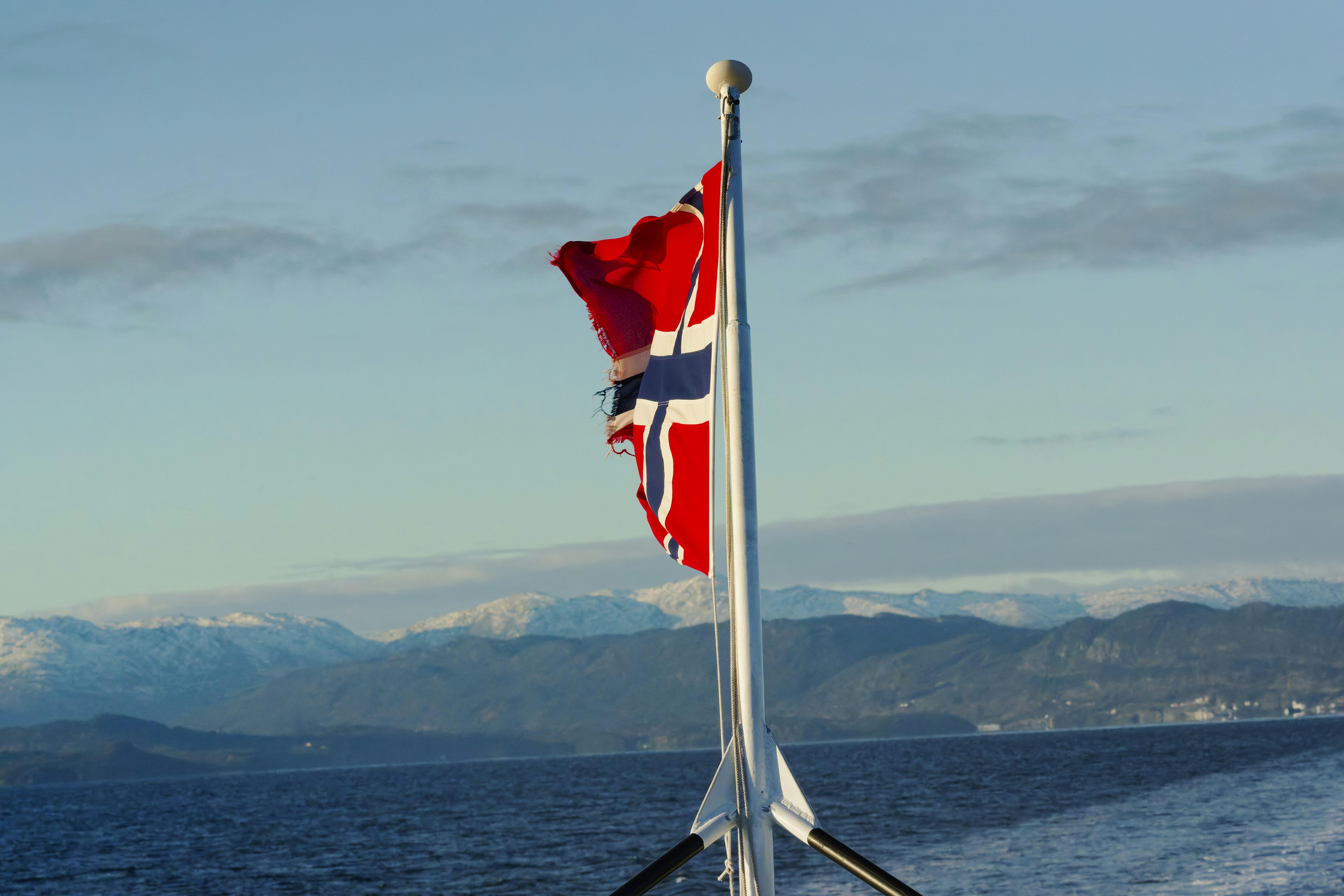 Norwegian flag waving on a pole over the ocean.