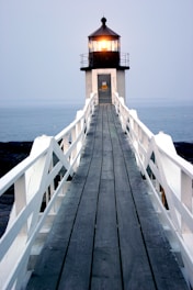 Wooden walkway leads to a lighthouse at dusk.