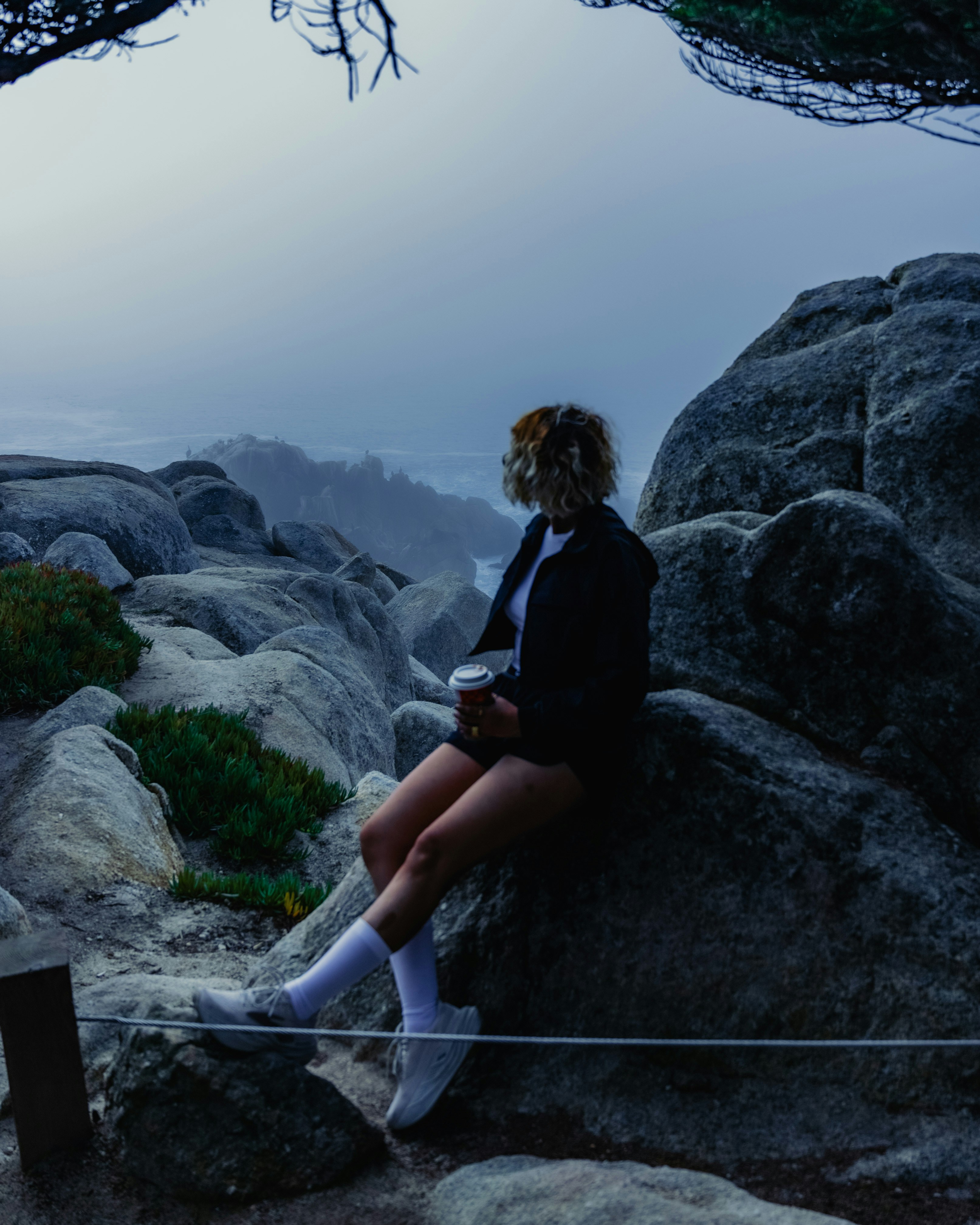 Woman sitting on rocks overlooking ocean