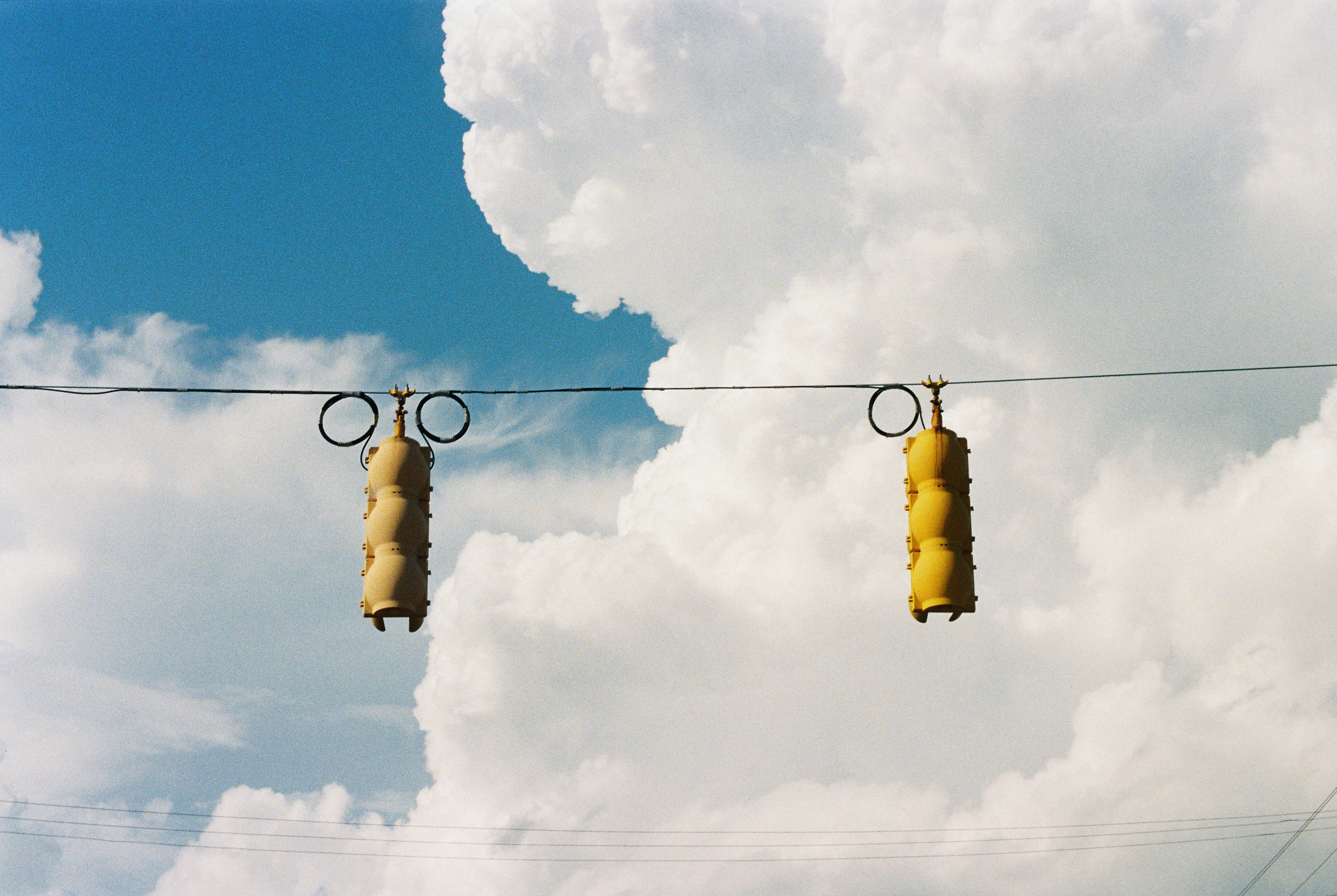 Two yellow traffic lights hang against a cloudy sky