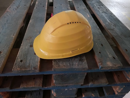 A yellow hard hat rests on a wooden pallet.