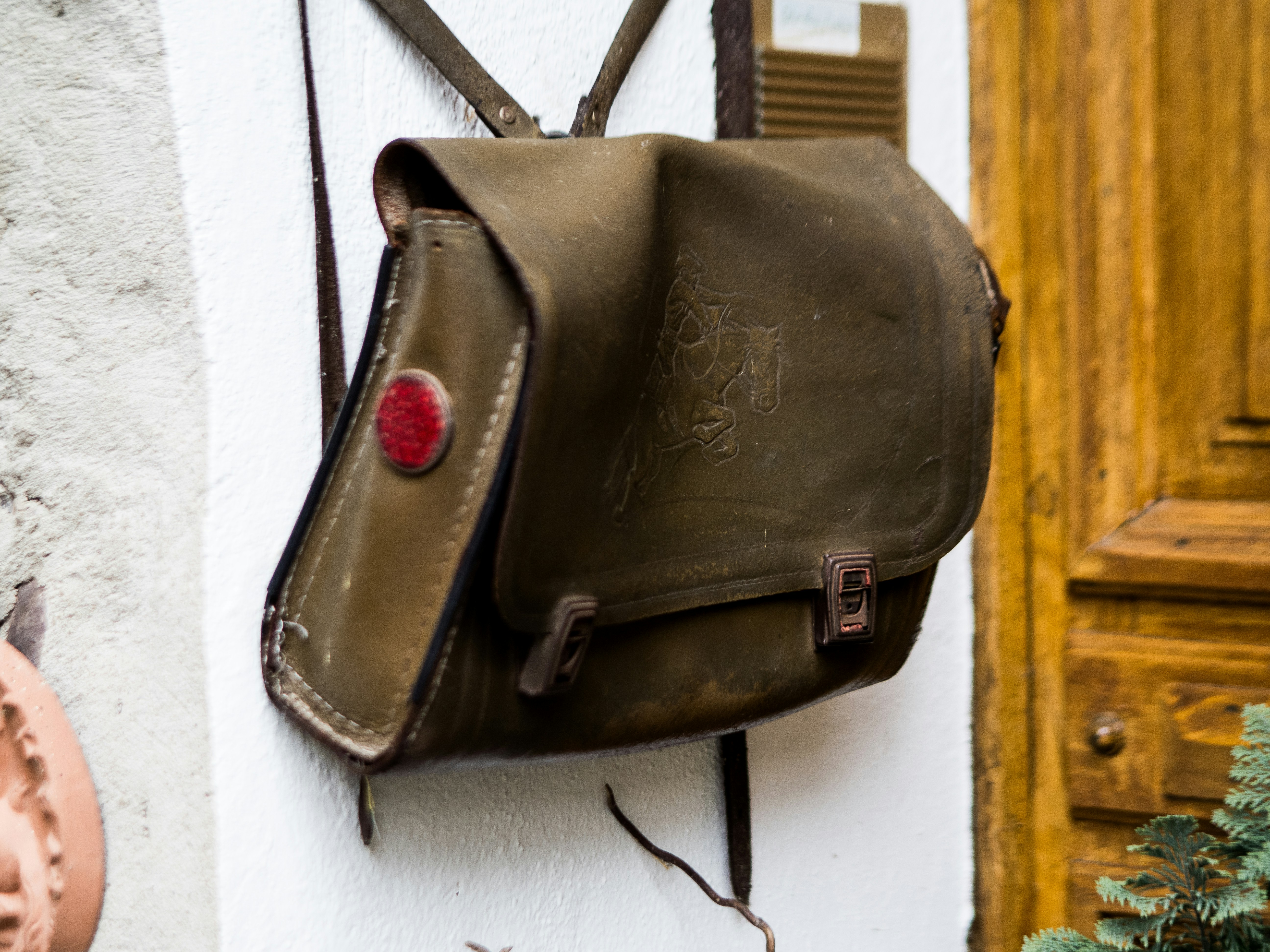 A vintage olive green satchel hangs on a wall.